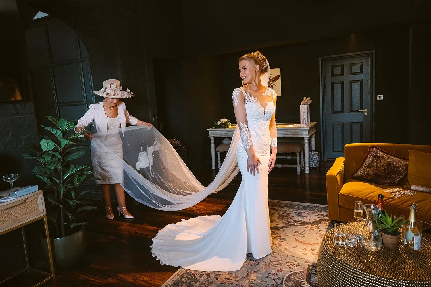 The Croft Hotel wedding: mother in a hat arranging the bride's long veil in a dark-panelled bridal suite.