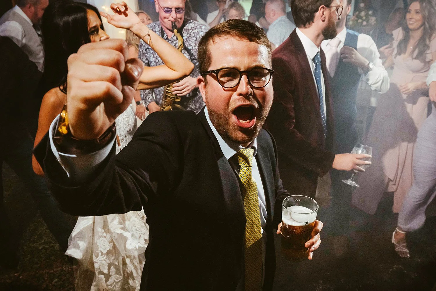 Beamish Hall wedding: guest in glasses with a fist raised and a pint in his hand celebrating on the dance floor