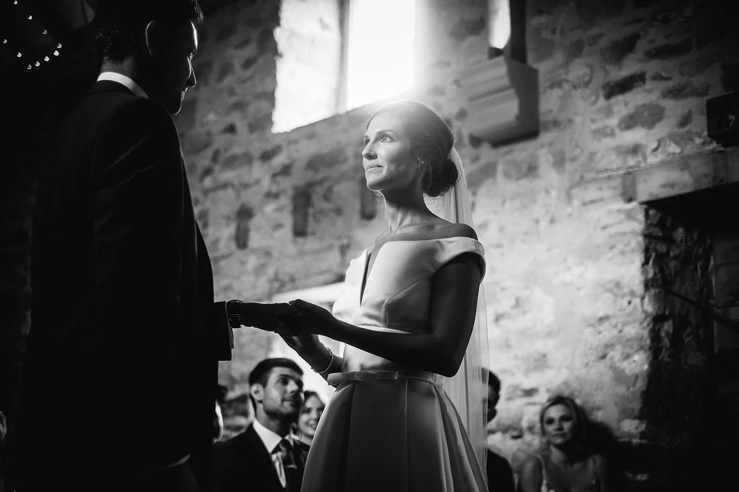 Healey Barn wedding: bride and groom exchanging rings in a stone ceremony room, black and white wedding photograph