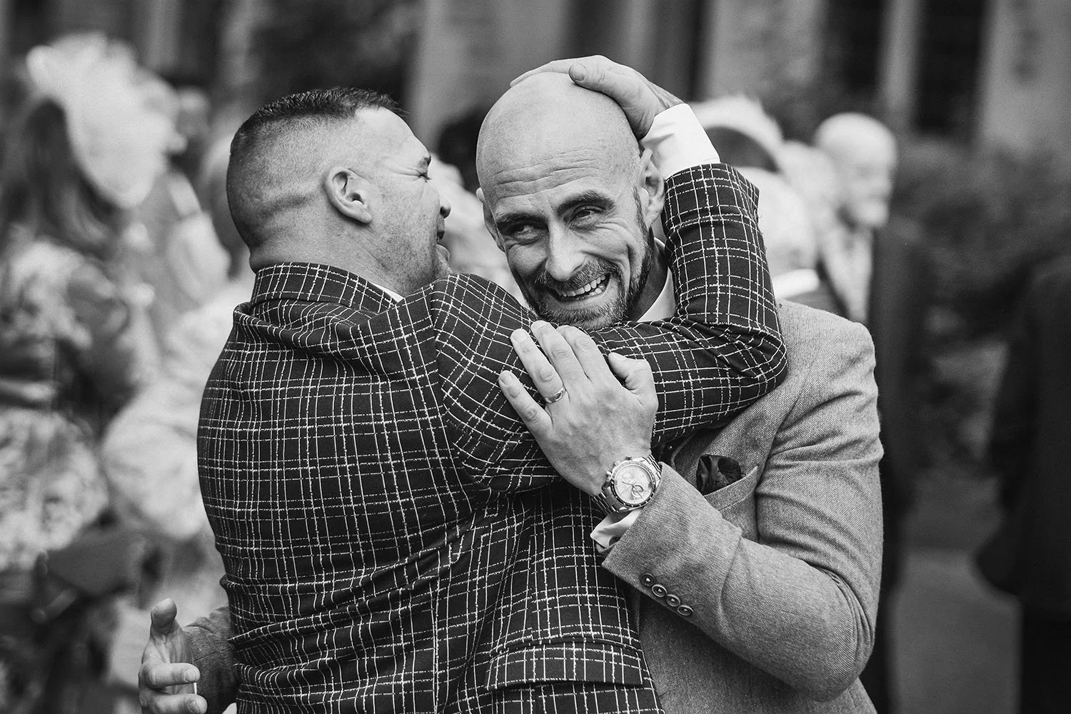 Jesmond Dene House wedding: two men in checked suits hugging and laughing together, in black and white.