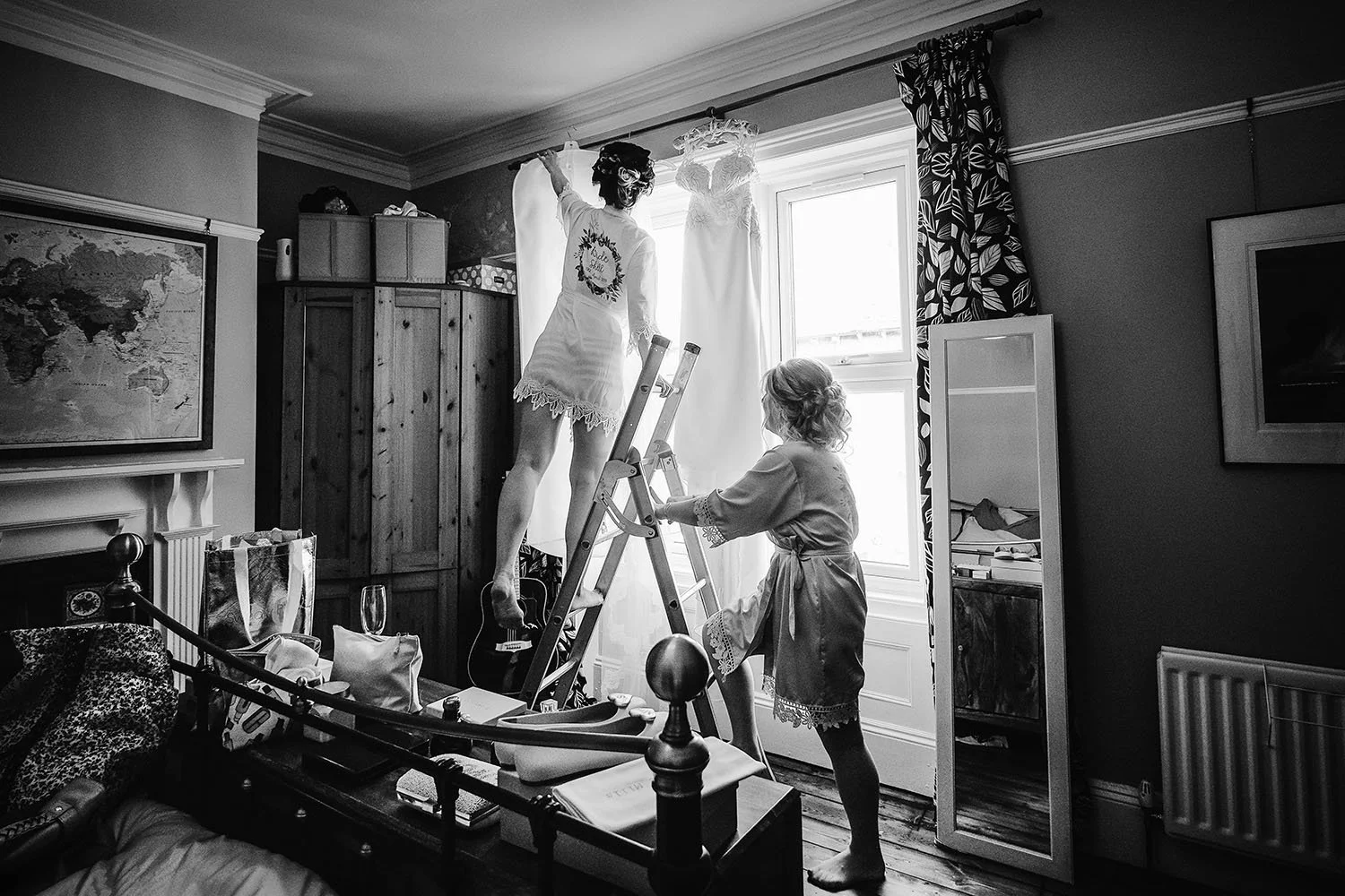 Northside Farm wedding: bride hanging up her wedding dress using a ladder in a bedroom, black and white