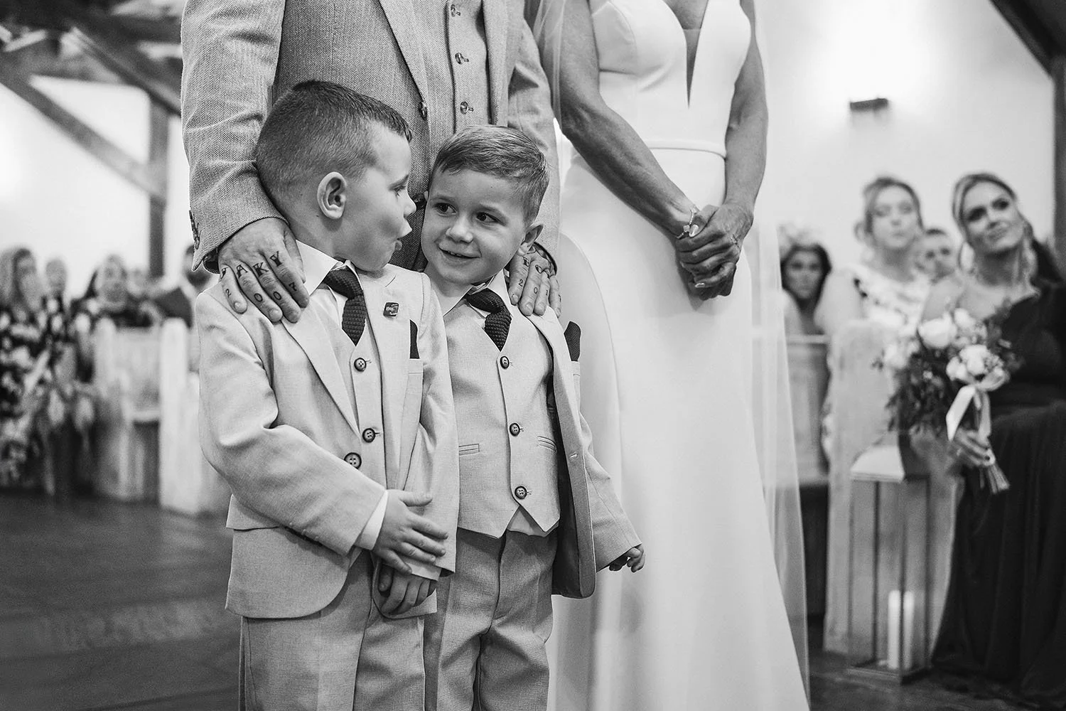 Two young boys in suits stand beside a bride and groom during a wedding ceremony as guests watch.