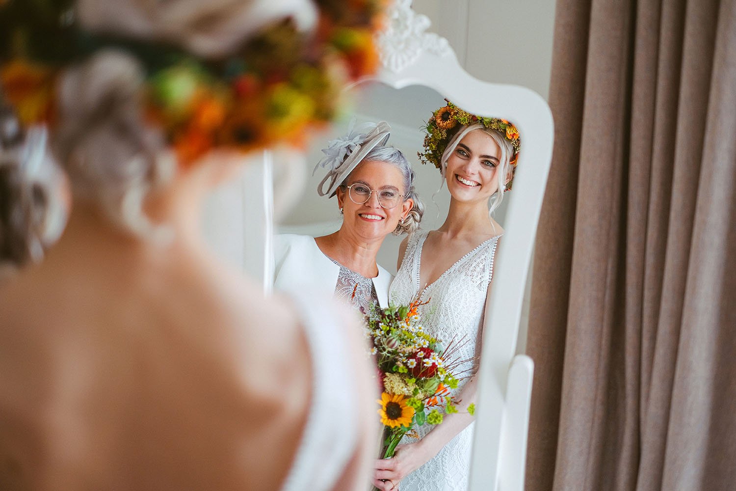 Hexham Winter Gardens wedding: bride in an autumn flower crown and her mother in a fascinator smiling in a white mirror