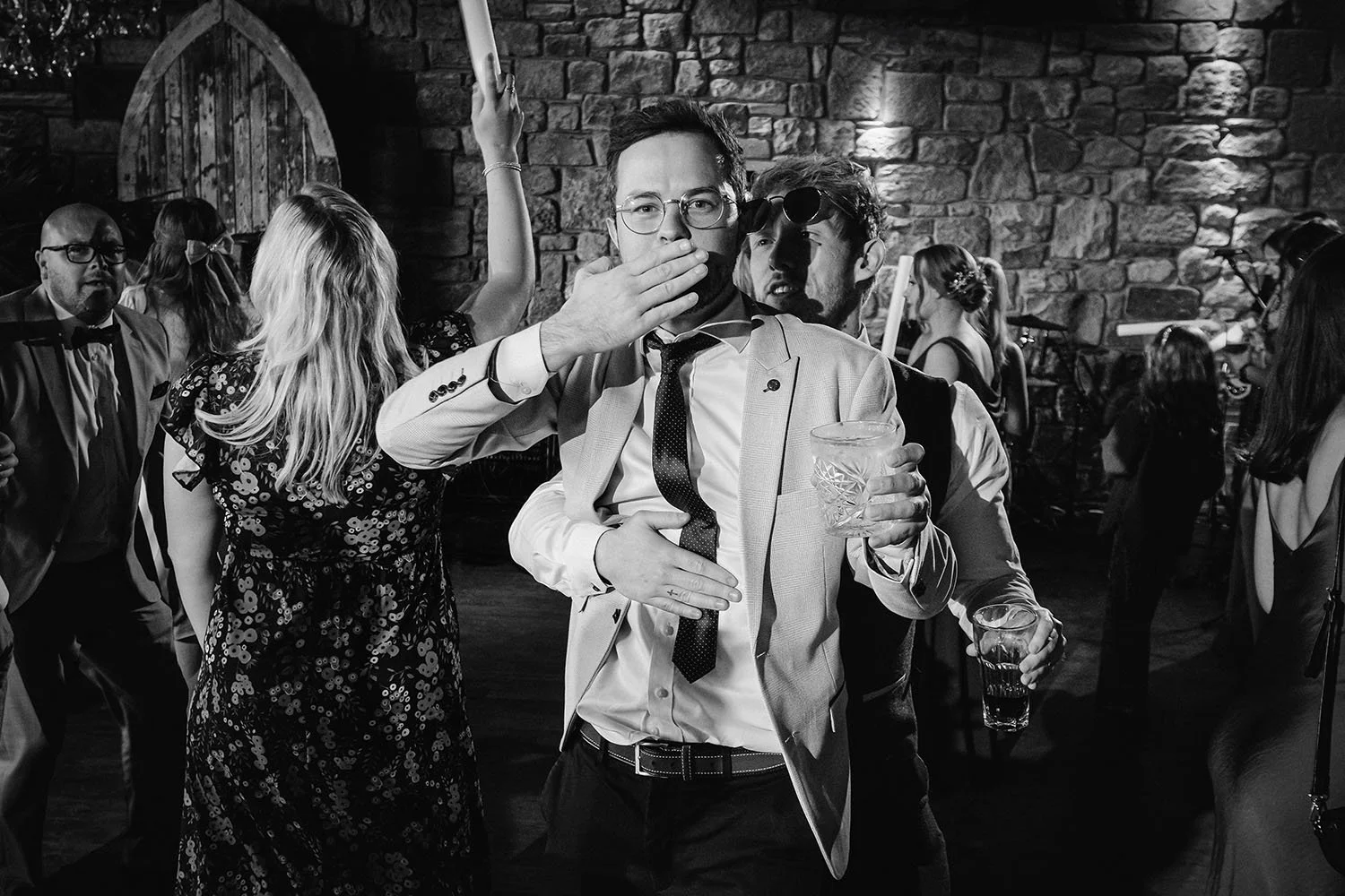Newton Hall wedding: guest in glasses with a loosened tie blowing a kiss as he dances with a drink in his hand