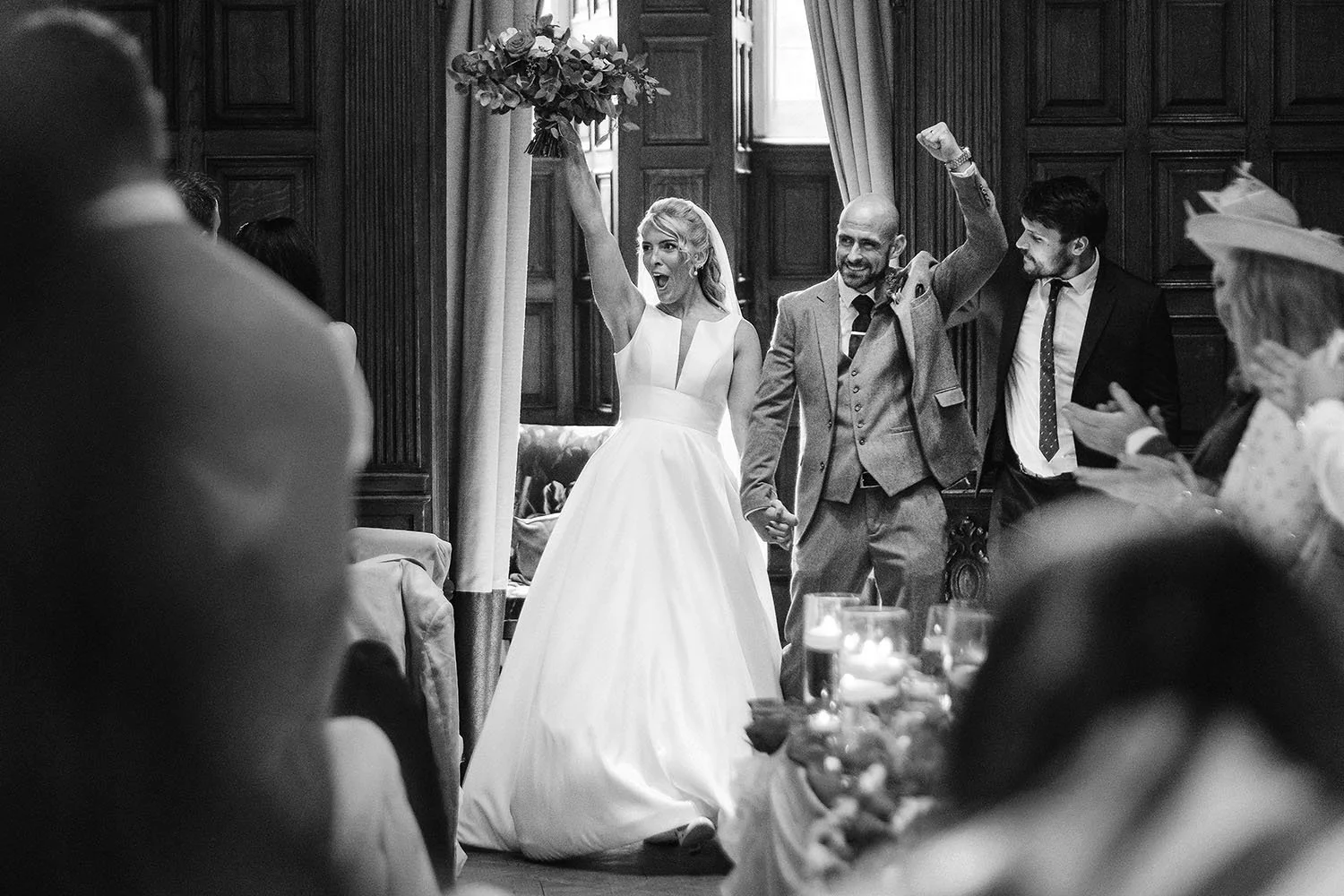 Jesmond Dene House wedding: bride holding her bouquet high and the groom with a fist raised as they enter the wedding breakfast