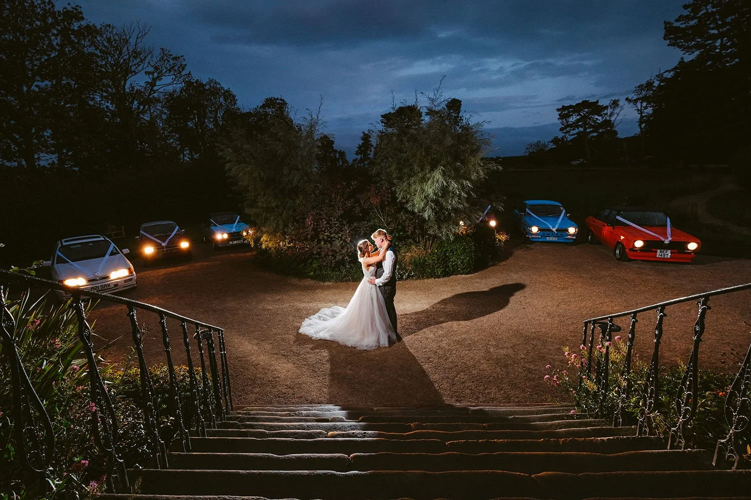 Newton Hall wedding: bride and groom embracing on a gravel drive at night below stone steps