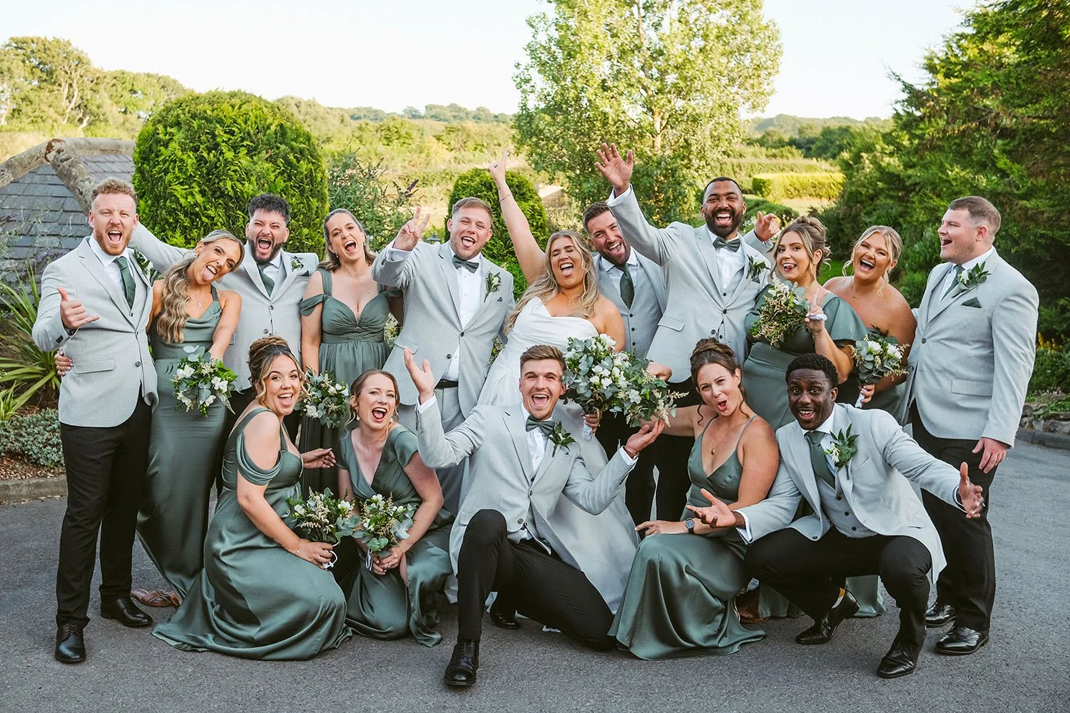 South Causey Inn wedding: bridal party in grey suits and sage dresses crouching and cheering together in a playful group portrait.