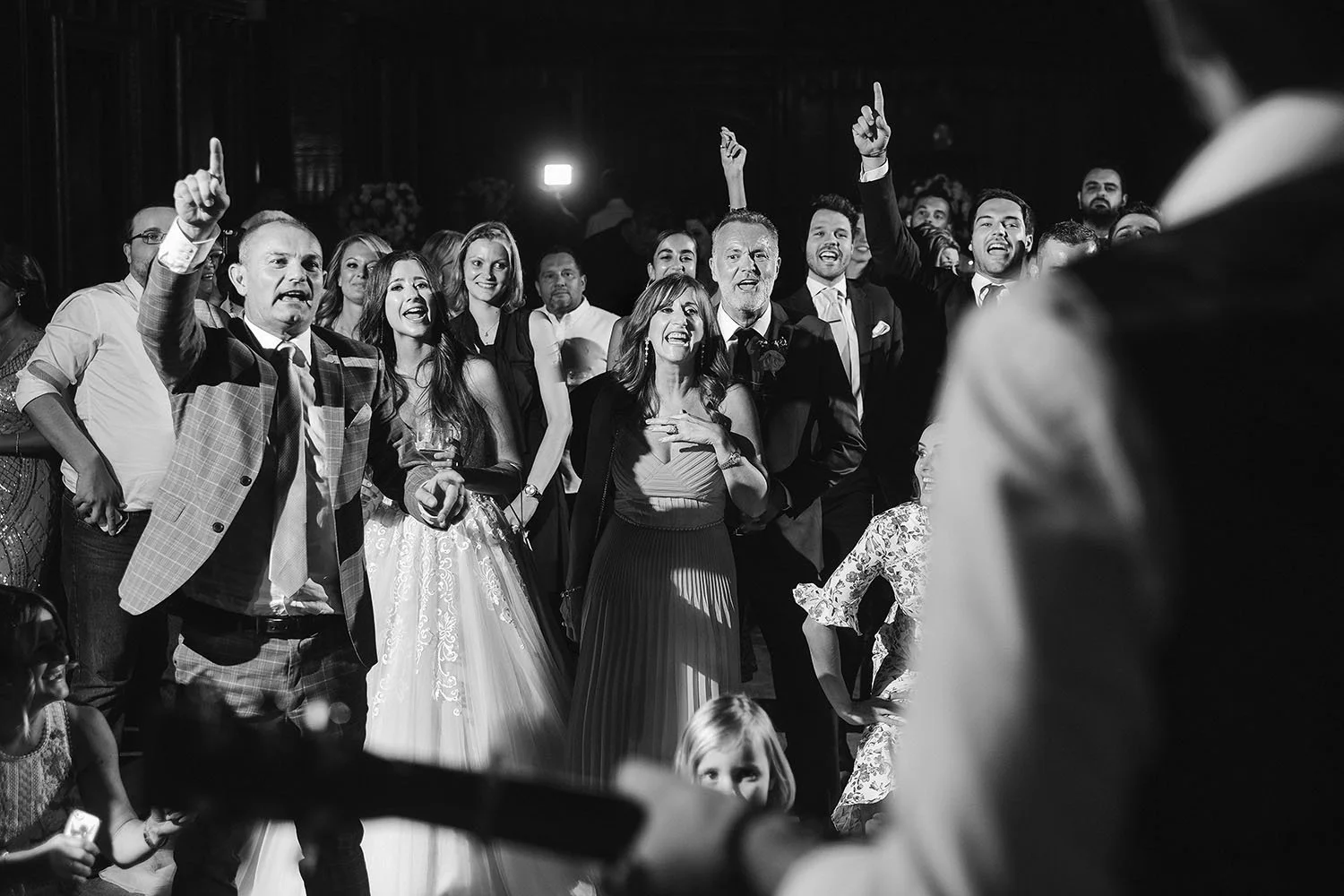 Durham Castle wedding: guests singing and pointing in the air around the bride on the dance floor, black and white