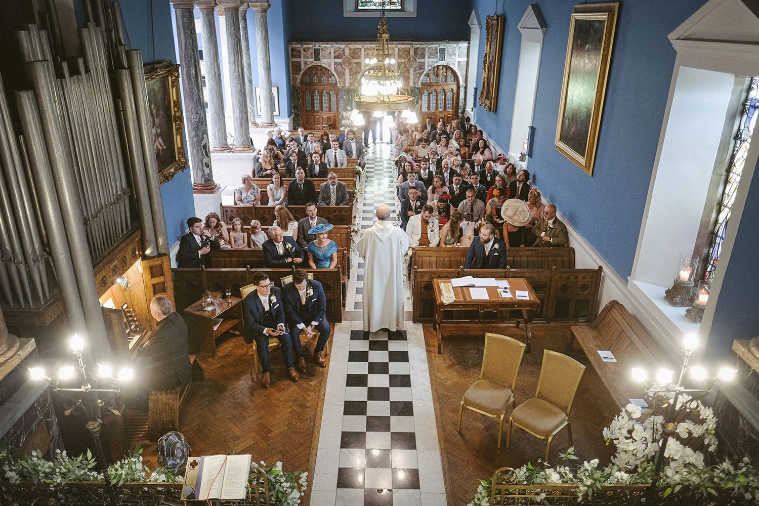 Wedding ceremony in a historic church with guests seated in wooden pews and a priest at the altar