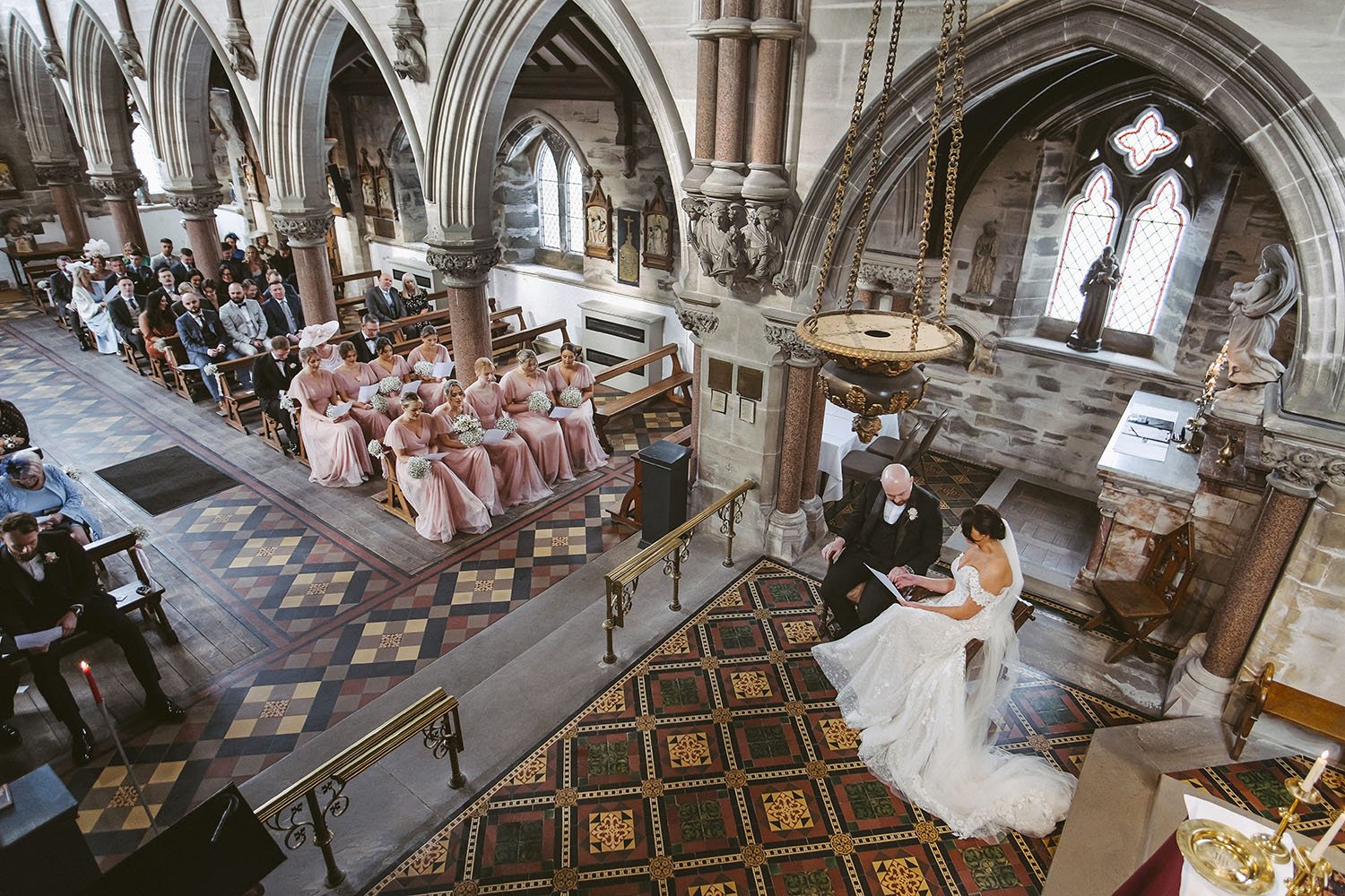 Rudding Park Hotel wedding: bride signing the register in a church seen from above, bridesmaids in pink seated in the pews.