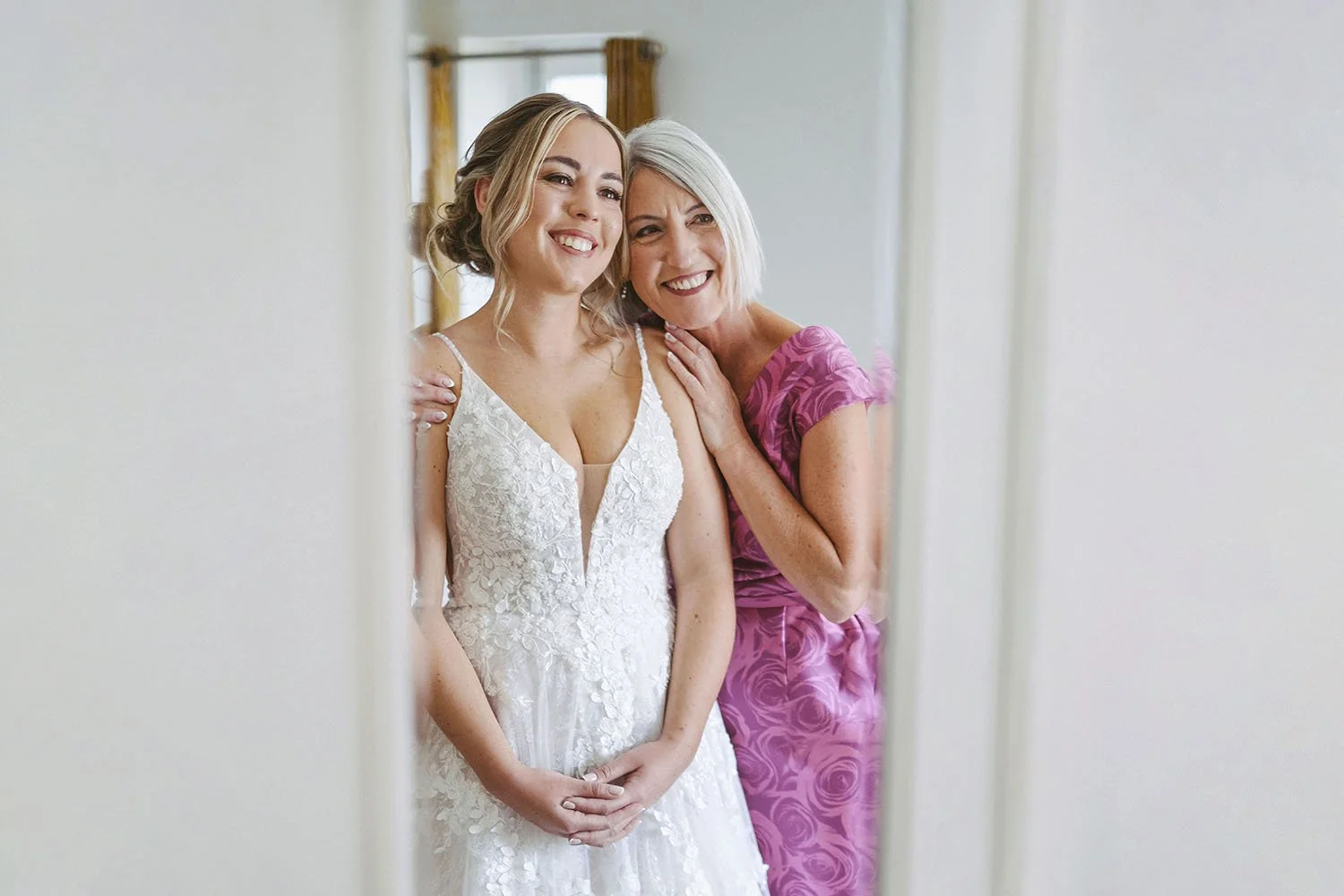 Beamish Hall wedding: the bride in lace and her mother in pink smiling together in a doorway.