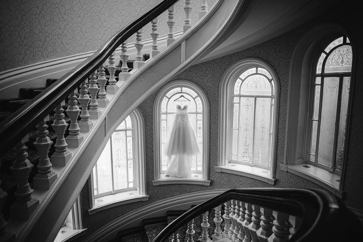 The Grand Hotel, Tynemouth wedding: wedding dress hanging in an arched window beside a curved staircase, black and white