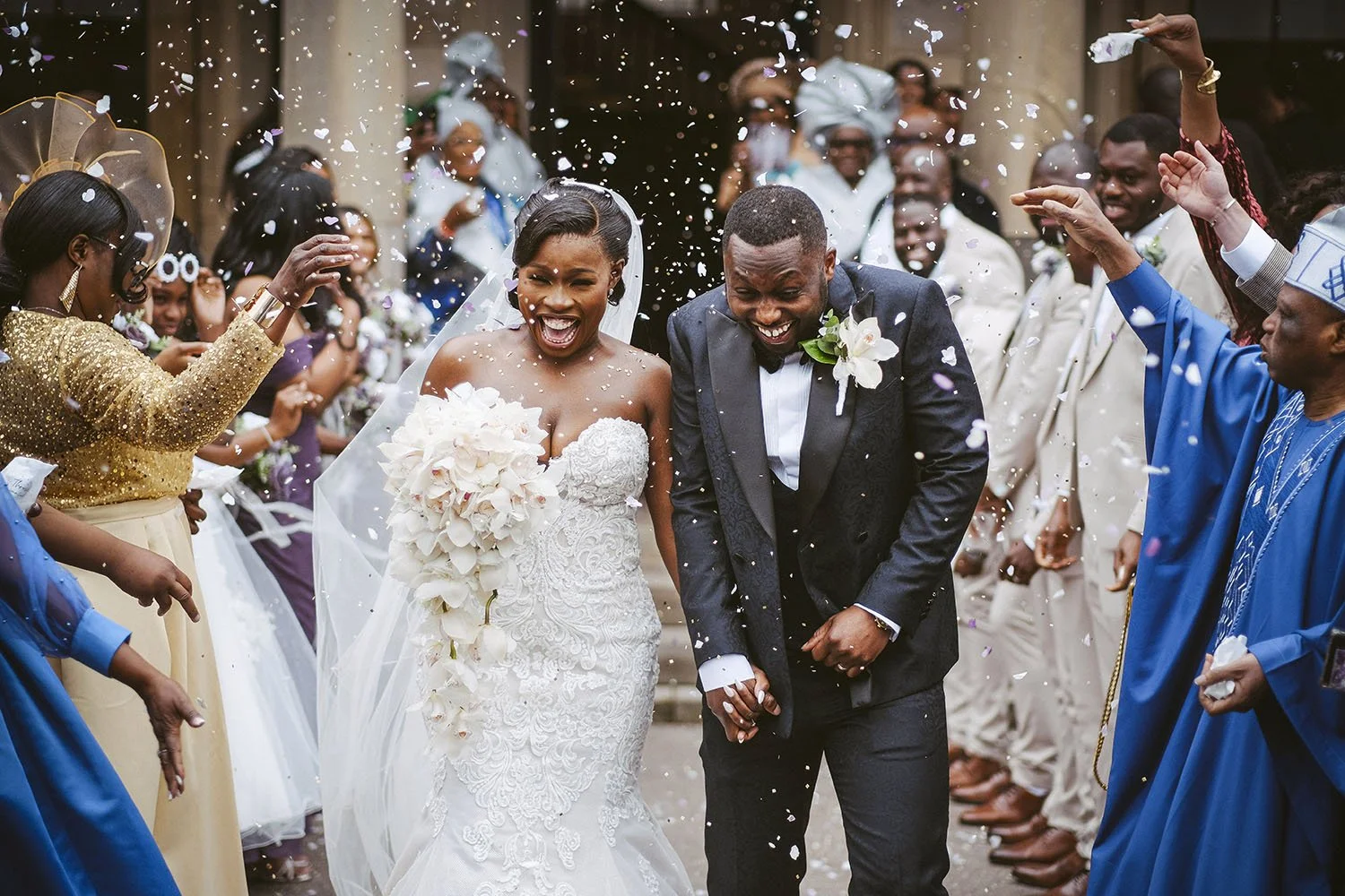 Beamish Hall wedding: bride and groom laughing as guests in colourful traditional dress throw confetti around them.