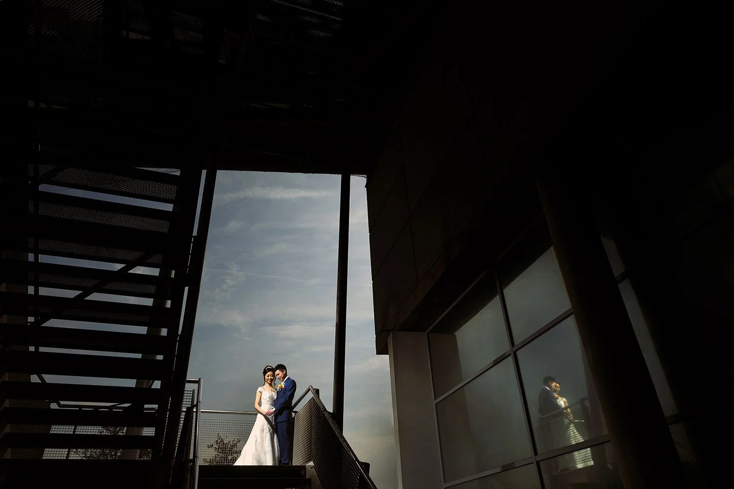National Glass Centre, Sunderland wedding: bride and groom embracing on a balcony beside a metal staircase against a dusk sky
