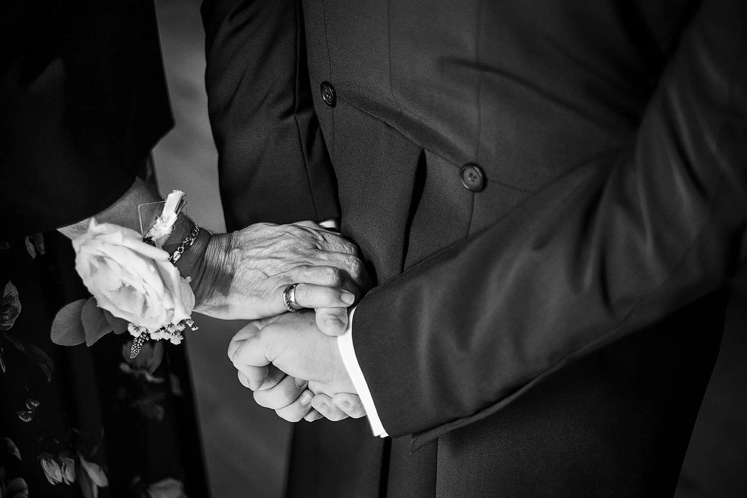 Eshott Hall wedding: close-up of two men shaking hands with a rose buttonhole on one wrist, black and white