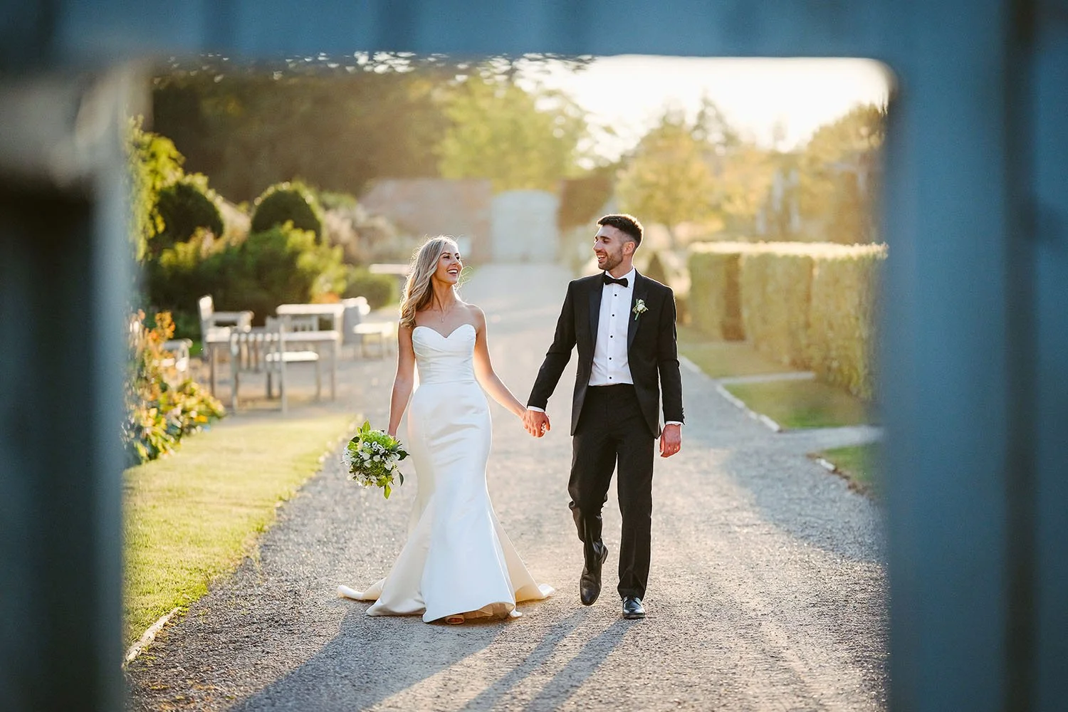 Wynyard Hall wedding: bride and groom walking along a sunlit gravel path, framed by a blue doorway.
