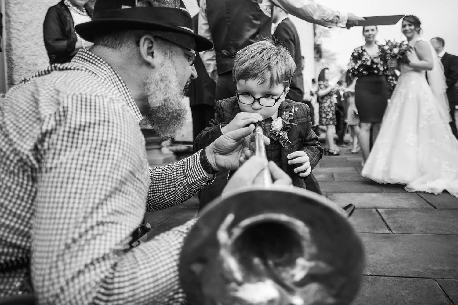 Black-and-white wedding photo of a bearded magician entertaining a young boy in glasses while the bride and guests watch