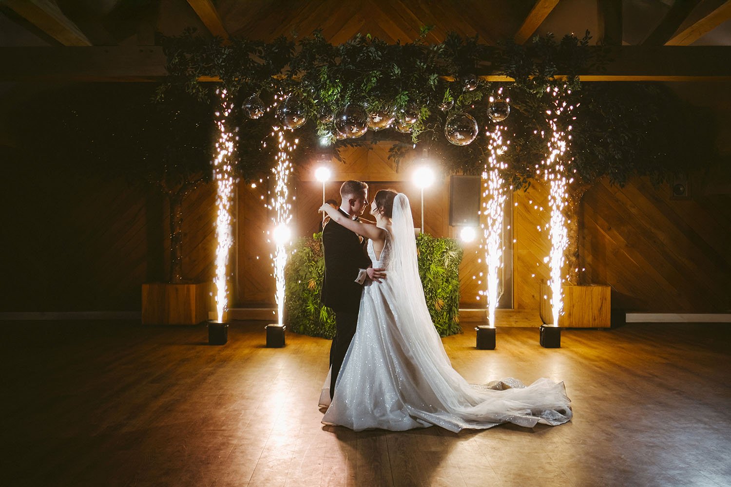 Doxford Barns wedding: bride and groom dancing in front of a greenery-covered wooden wall with cold spark fountains