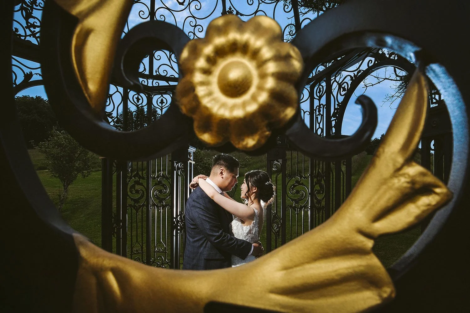 The Black Horse, Beamish wedding: bride and groom embracing in front of an ornate iron gate, framed by a gold flower detail.