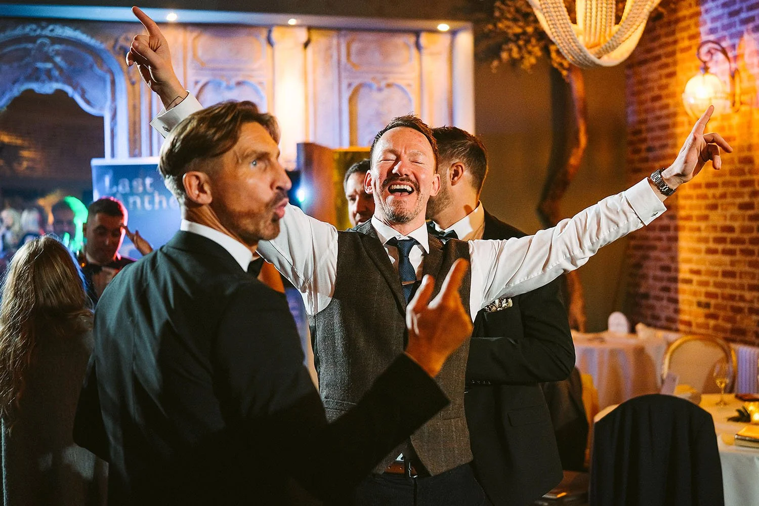 The Croft Hotel wedding: guest in a tweed waistcoat singing with his arms wide as friends point upwards at the party.