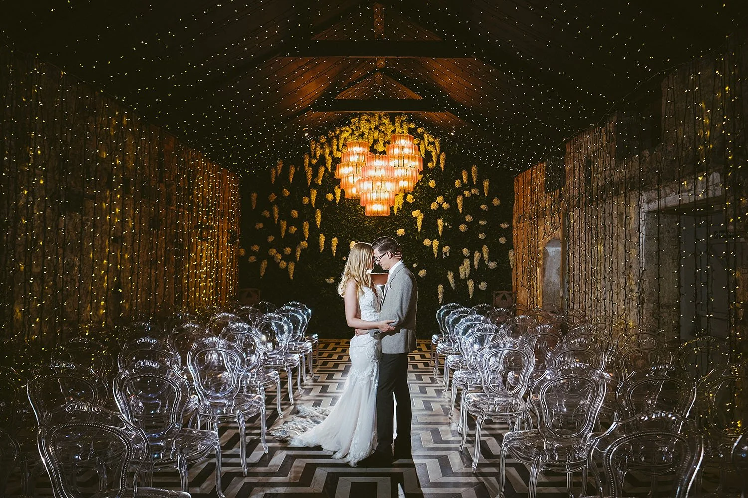 Charlton Hall wedding: bride and groom embracing in a barn with a curtain of fairy lights