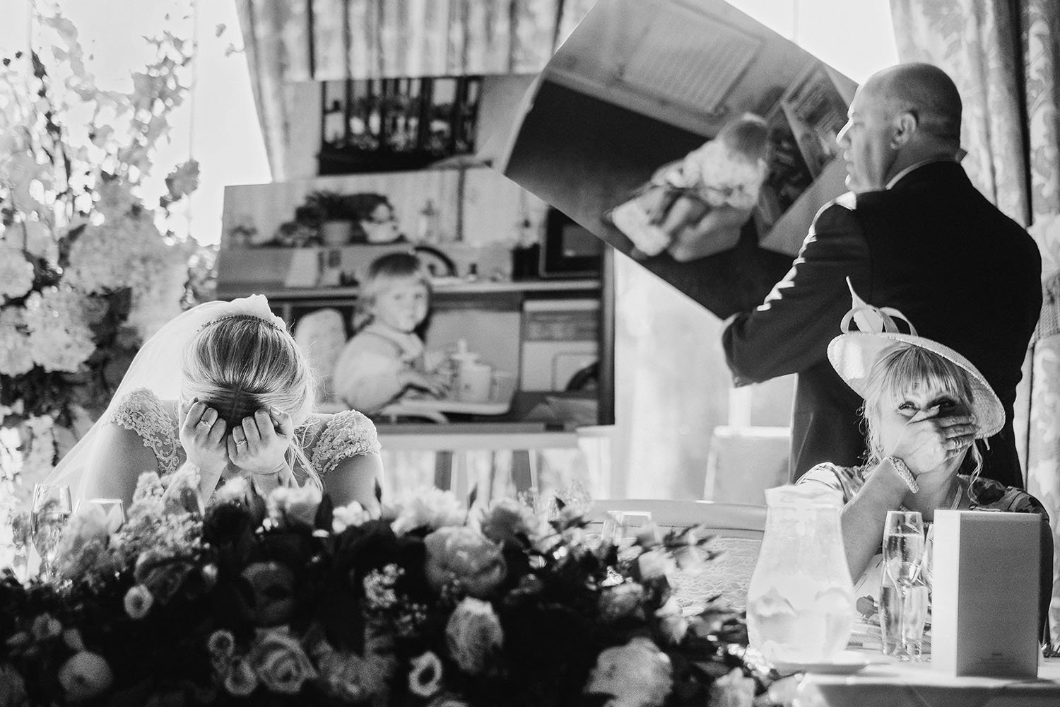Wynyard Hall wedding: bride covering her face in tears during a wedding speech with a photo slideshow behind, black and white