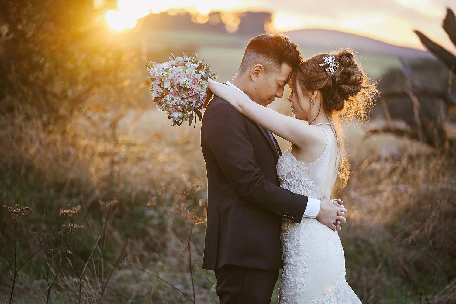 Le Petit Chateau wedding: bride and groom embracing forehead to forehead in a golden field at sunset.
