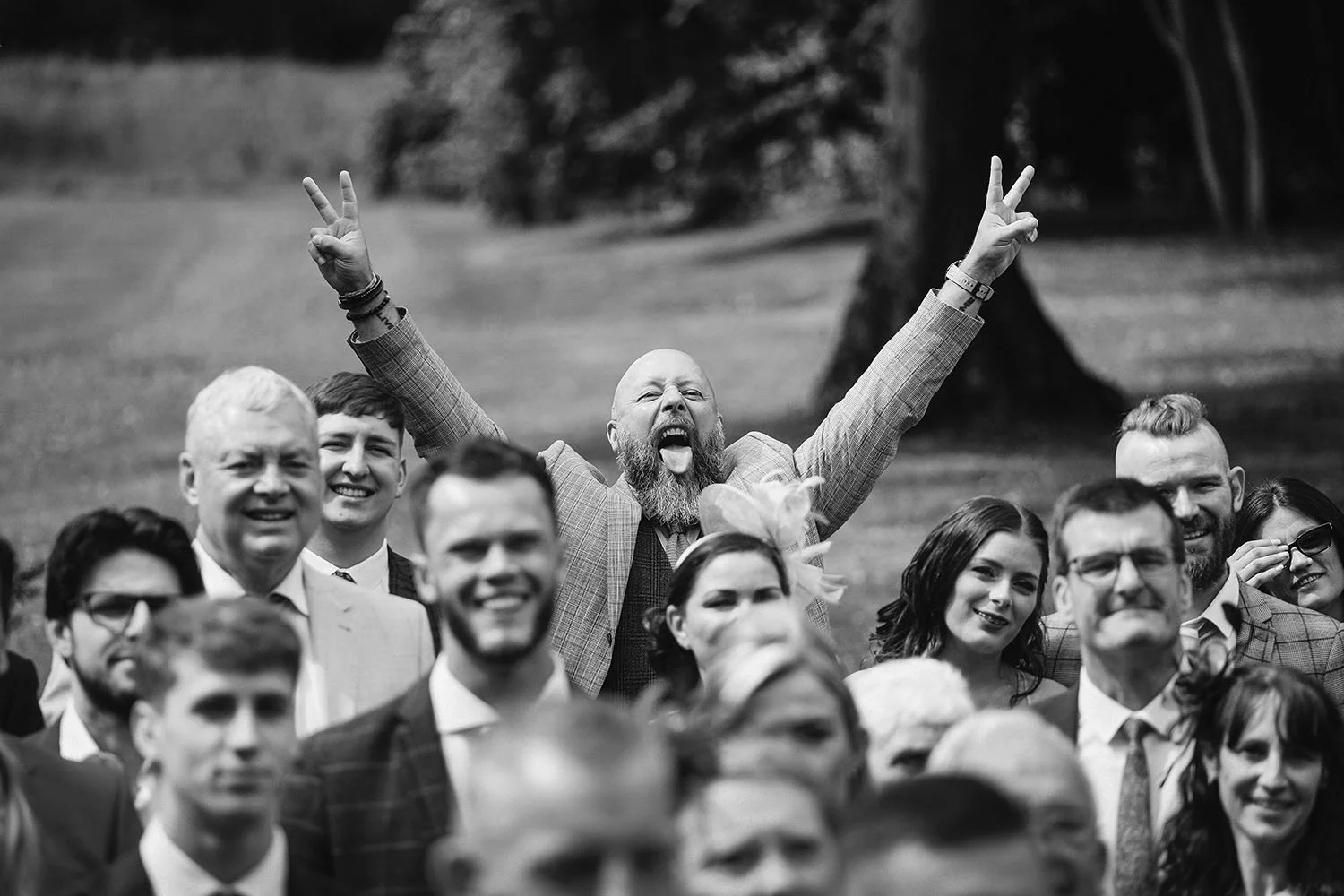 Beamish Hall wedding: crowd of guests cheering, one man with his arms in the air and tongue out, in black and white.
