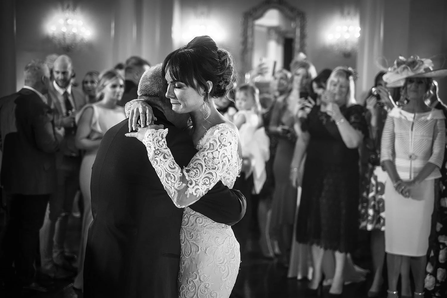 Bride and groom embracing during a wedding reception as guests watch and take photos