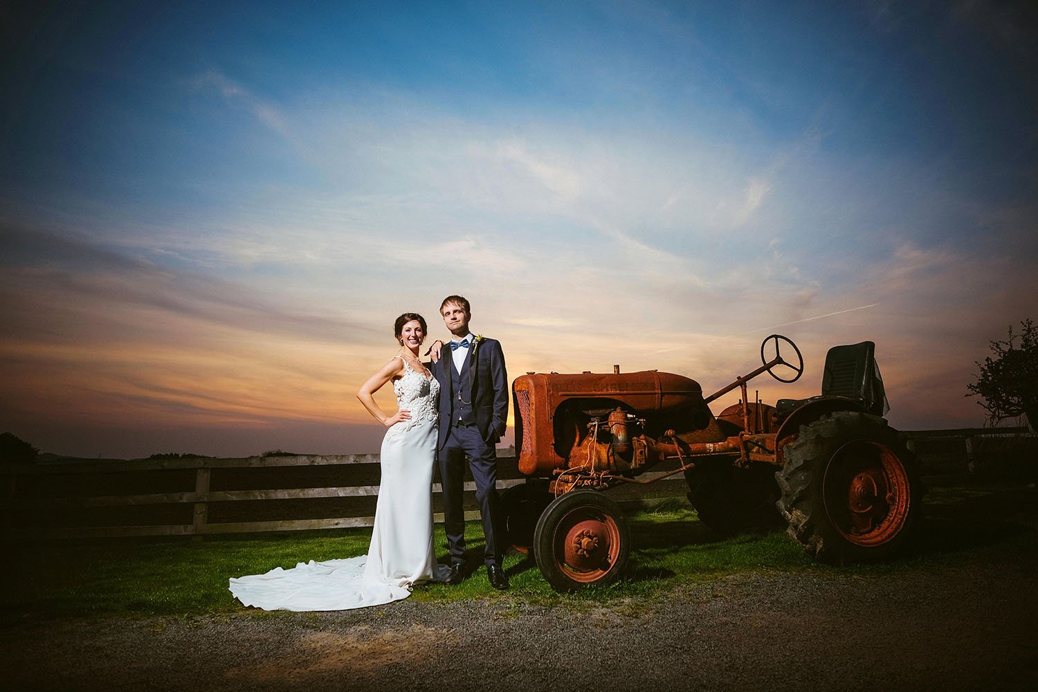 Northside Farm wedding: bride and groom standing beside a vintage red tractor at sunset