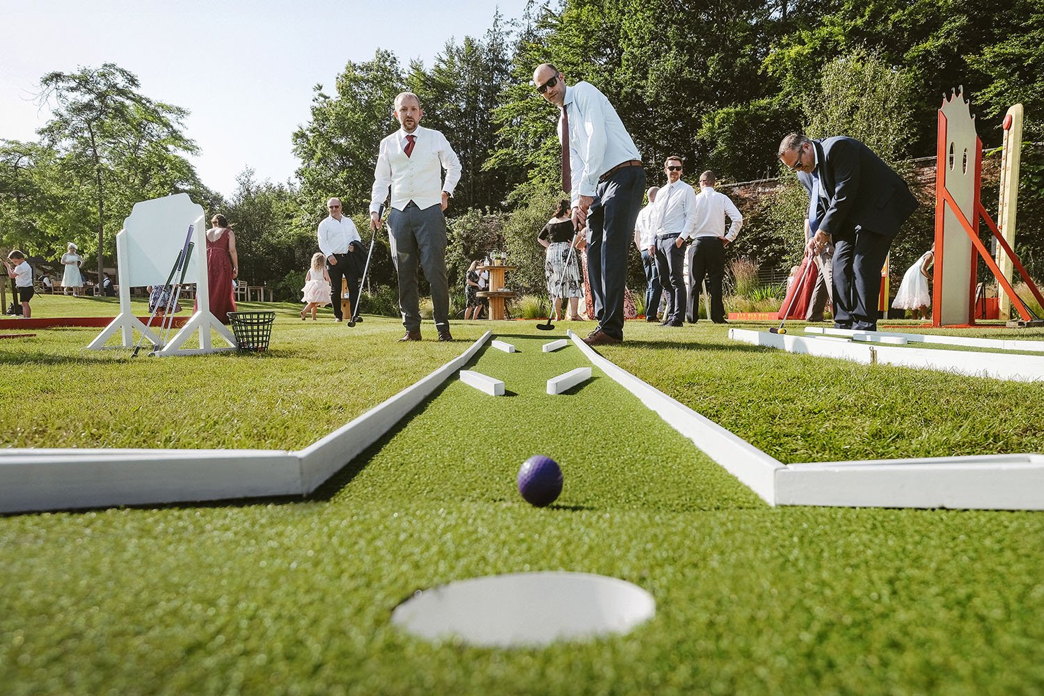 Alnwick Garden wedding: wedding guests playing crazy golf on a lawn, a ball on the green in the foreground.