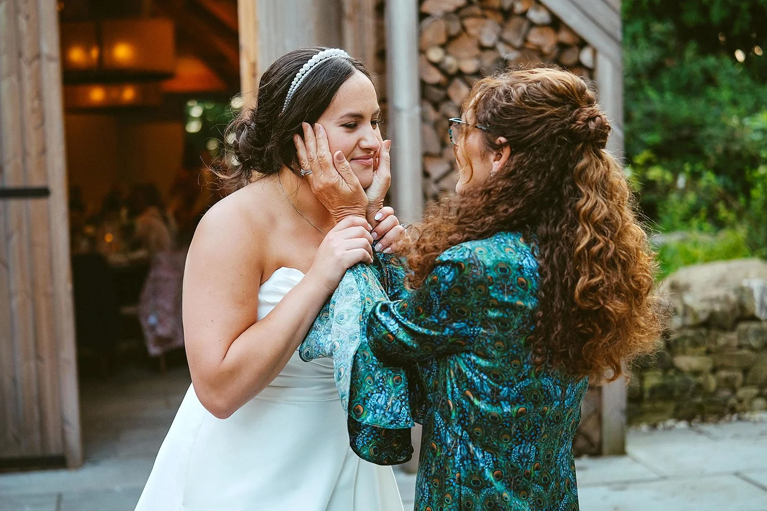 Halton Grove wedding: bride in a headband laughing as a guest in a peacock-print top holds her face in her hands outside a barn.