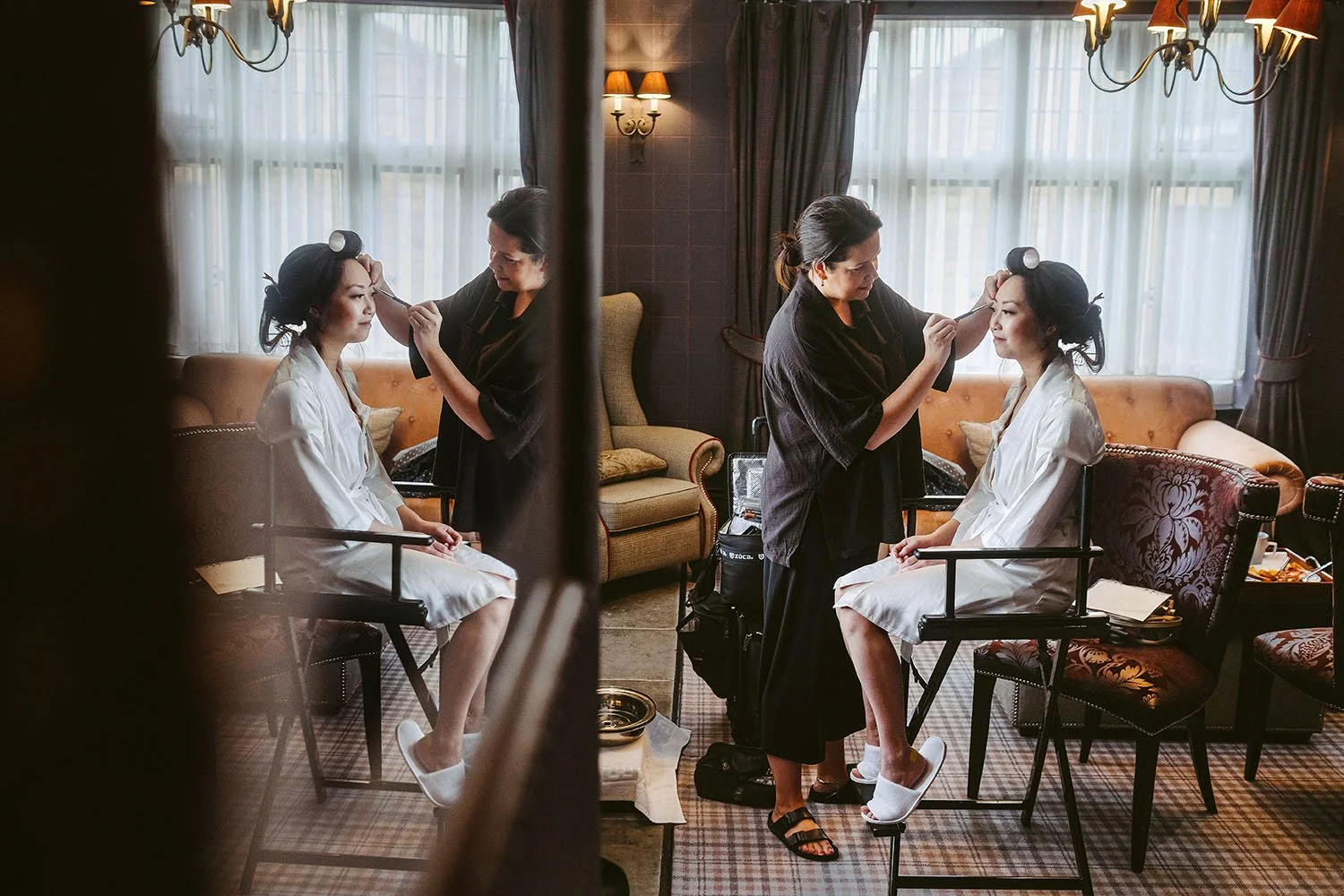 Bride and bridesmaid having hair and makeup done in a lounge with large windows.