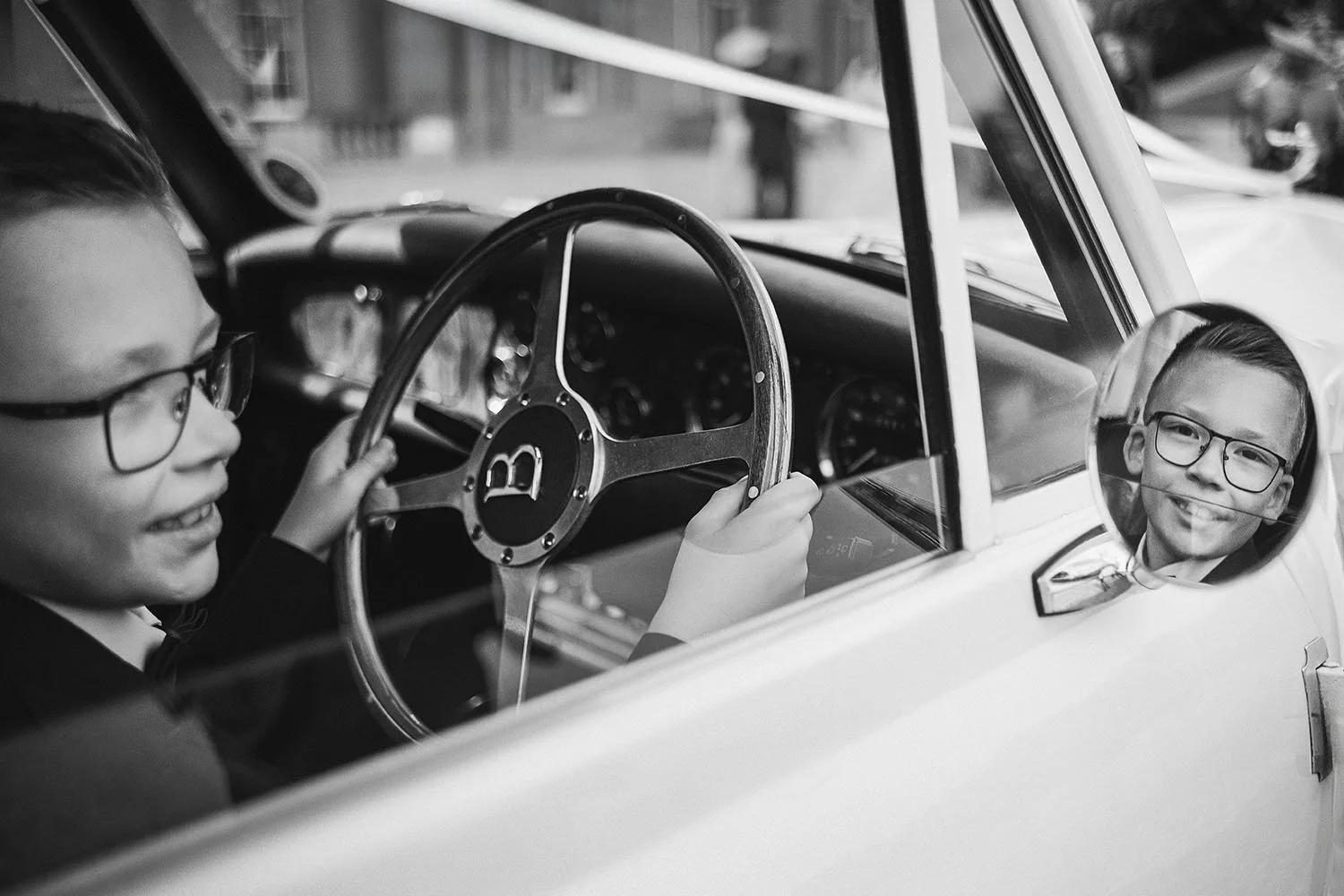 Wynyard Hall wedding: smiling boy in glasses sitting at the wheel of a vintage car, his face reflected in the wing mirror