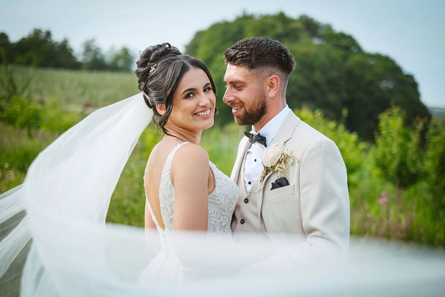 South Causey Inn wedding: bride smiling over her shoulder at the camera as the groom in a cream suit looks at her