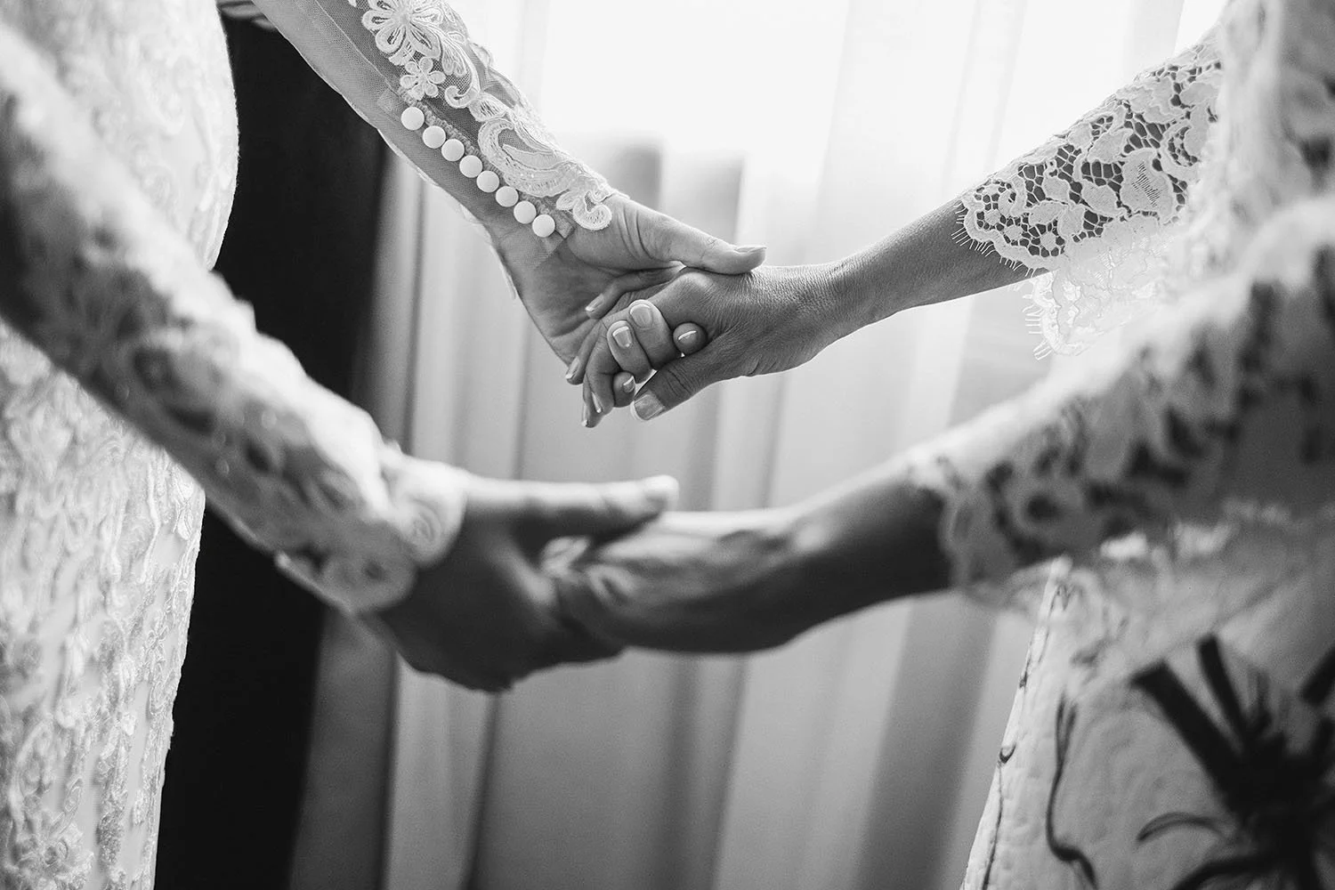 Ramside Hall wedding: close-up of two hands clasped in lace sleeves, one with buttoned cuffs, in black and white.