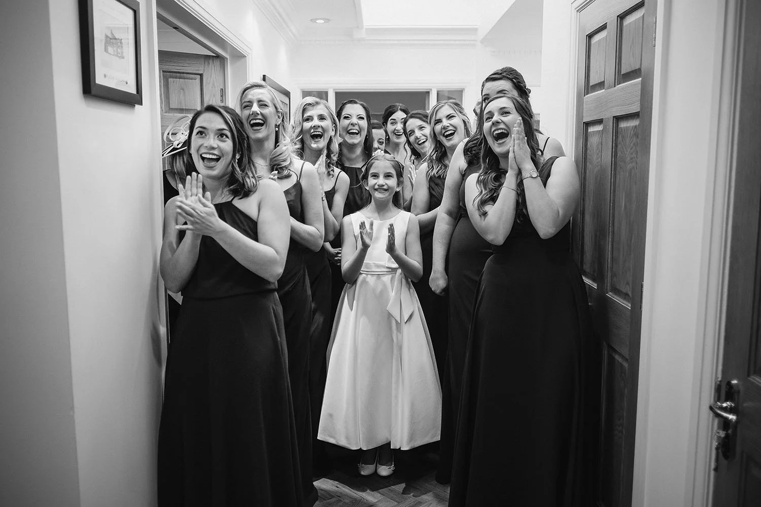 Bridesmaids and a flower girl cheering and clapping in a doorway, in black and white.