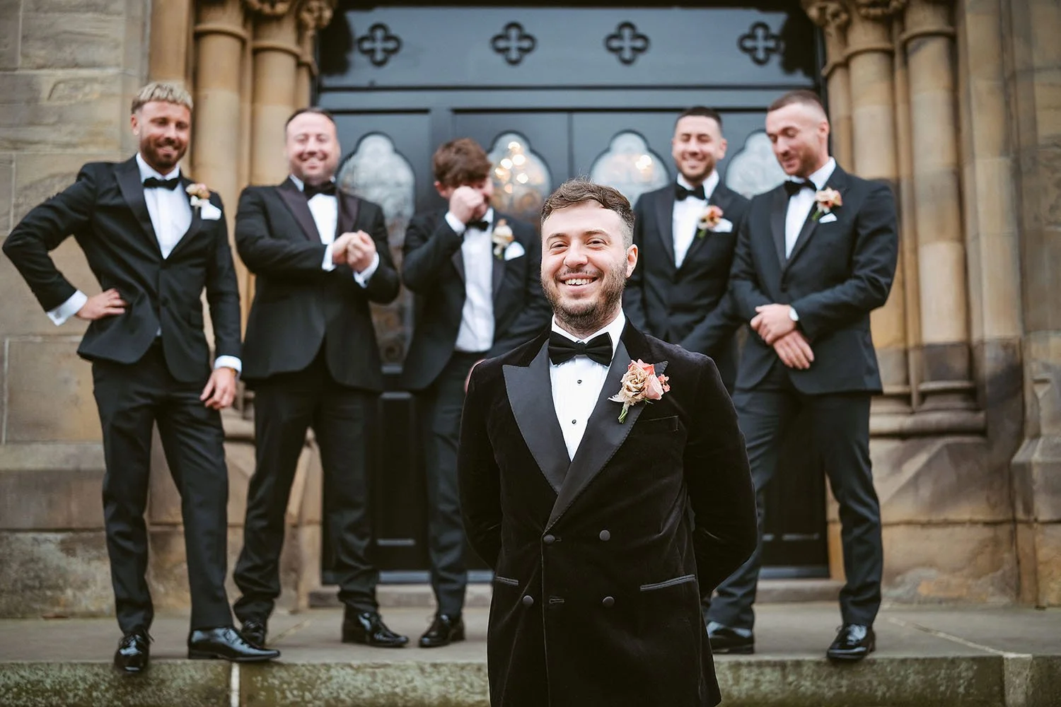 Dalton Pump House wedding: groom in a velvet jacket laughing at the camera while five groomsmen in tuxedos pose