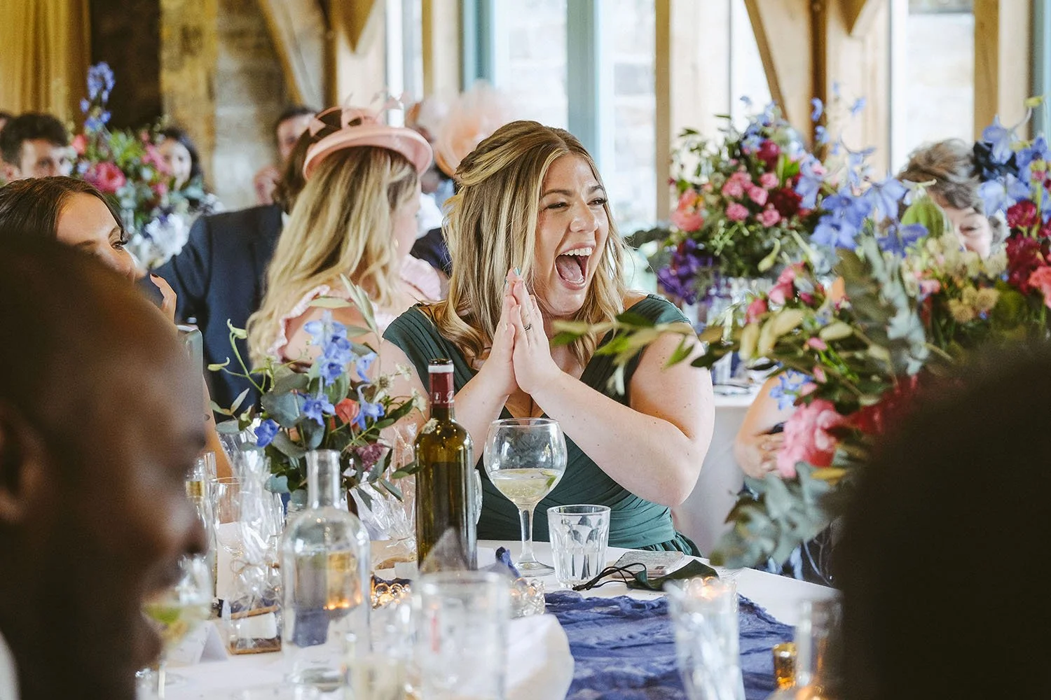 Healey Barn wedding: wedding guest laughing and clapping at a table decorated with colourful flowers.
