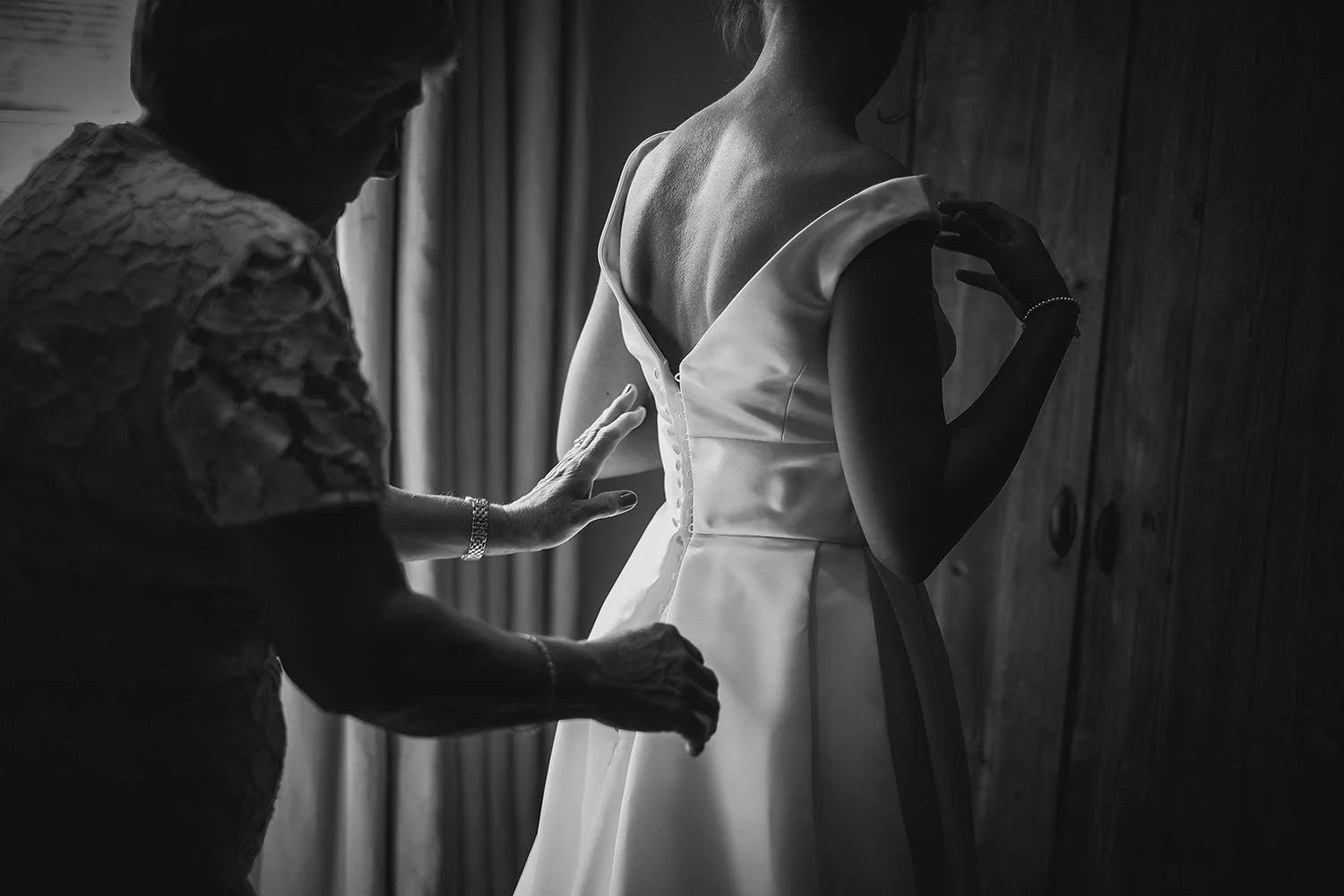 Healey Barn wedding: mother helping the bride with the buttons on her satin wedding dress, black and white