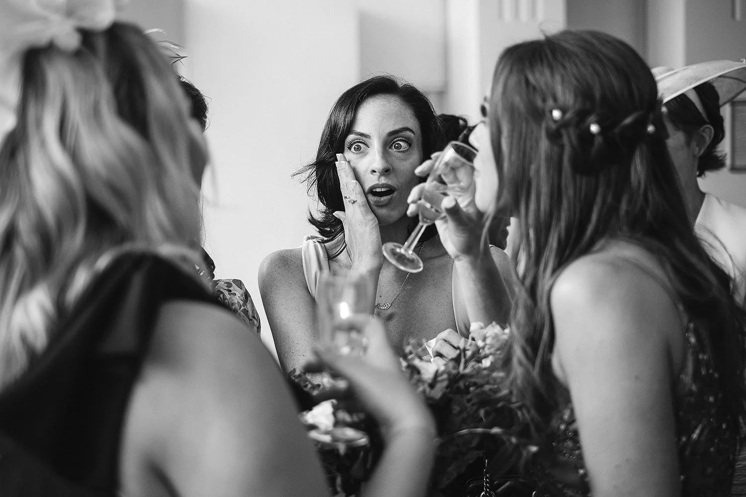 Beamish Hall wedding: bridesmaid with a surprised expression holding a champagne glass among guests, in black and white.