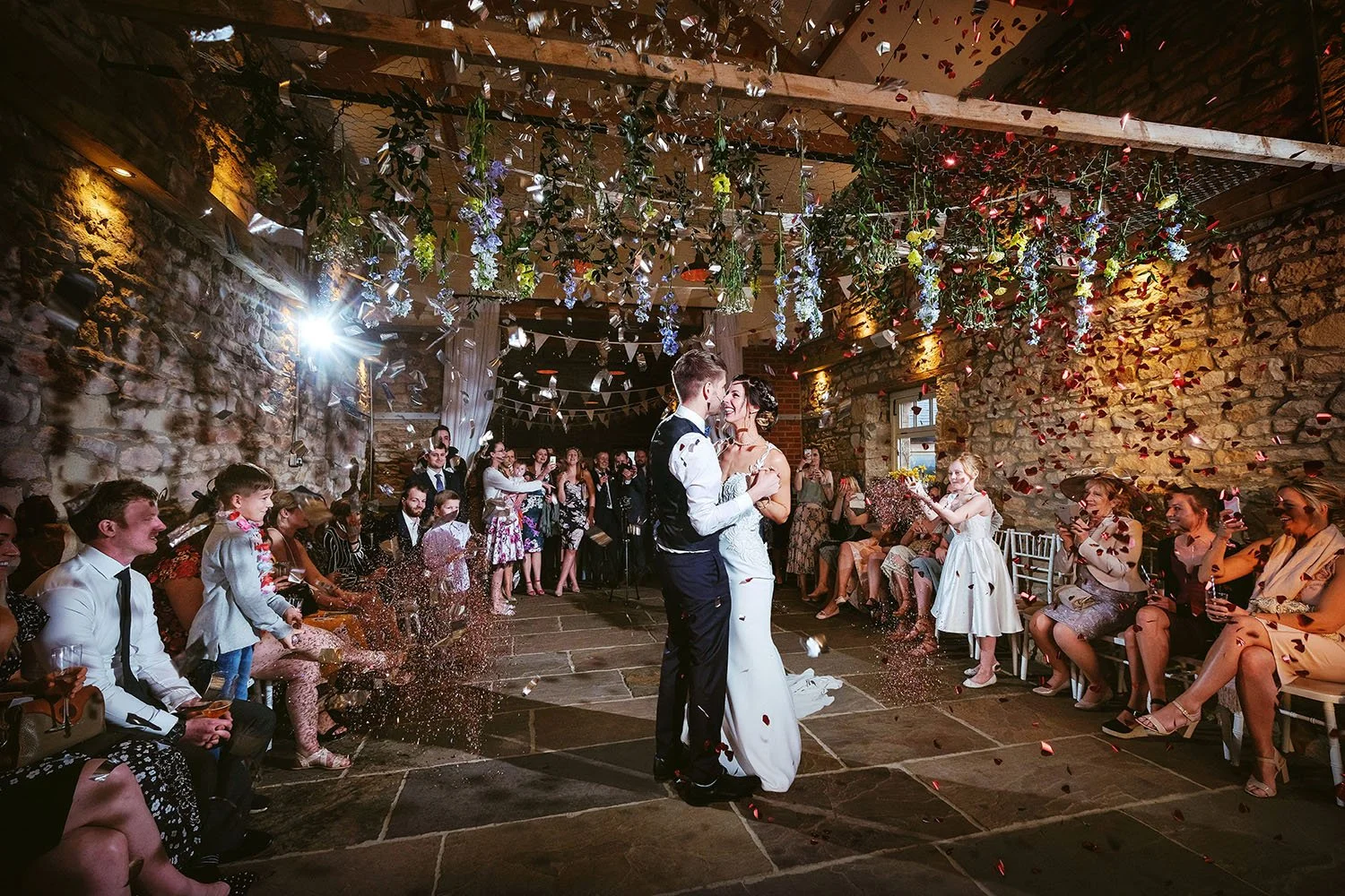Northside Farm wedding: bride and groom first dance as petals fall from a flower-covered barn ceiling