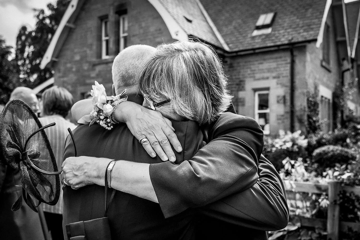 Eshott Hall wedding: wedding guests sharing an emotional hug outside a house, black and white