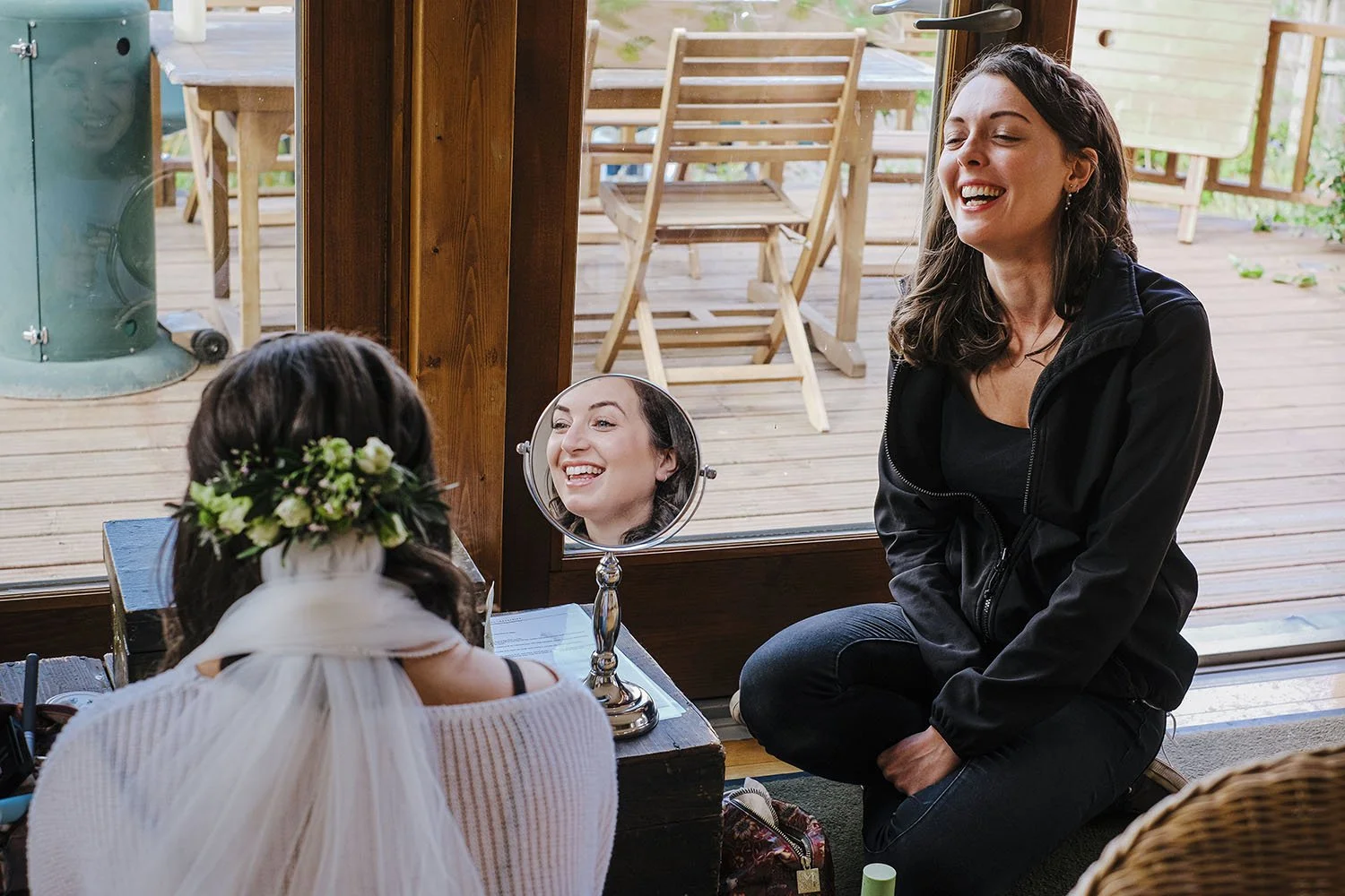 Auckland Castle wedding: bride in a floral hair wreath and a laughing guest reflected in a small hand mirror