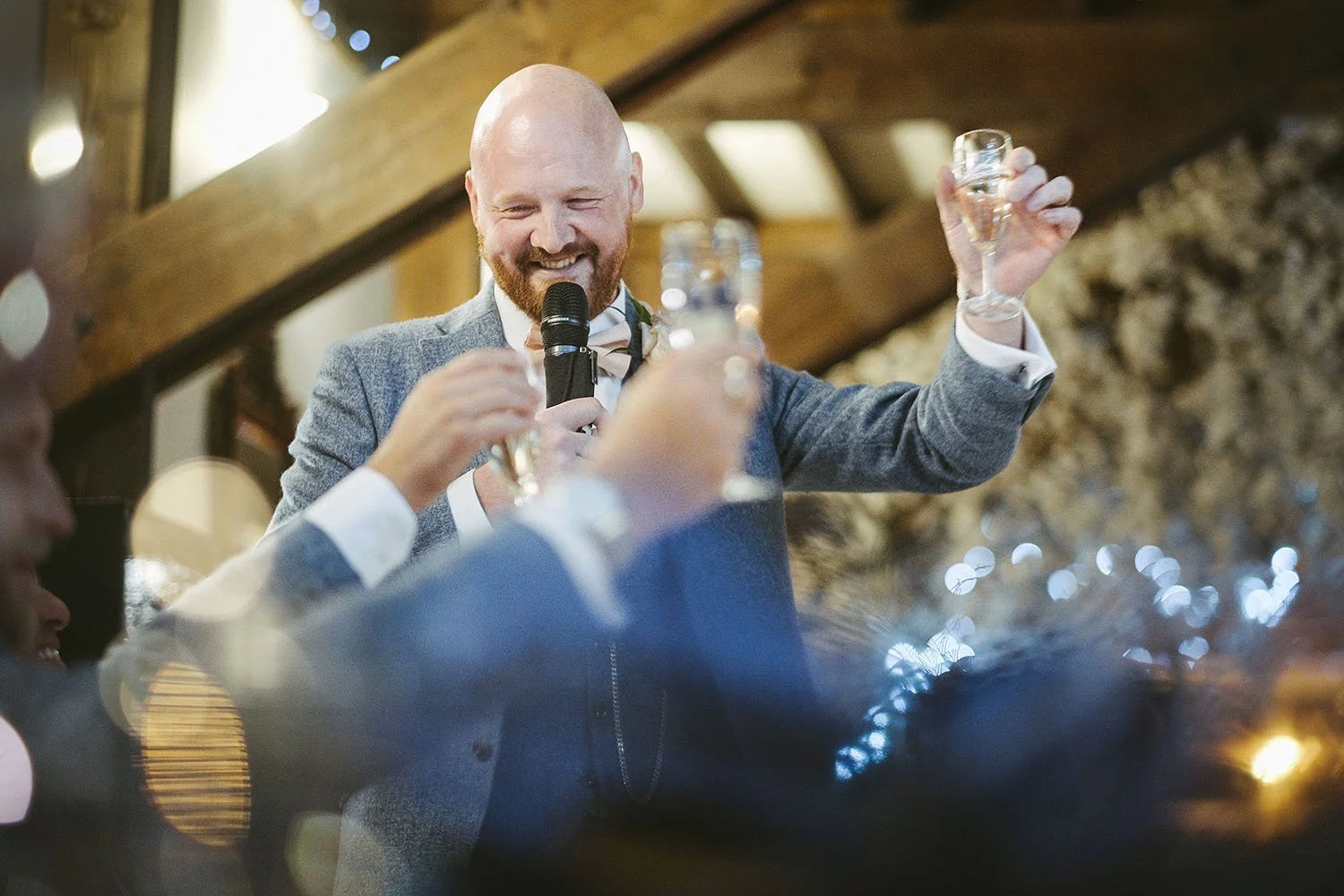 South Causey Inn wedding: best man holding a microphone and raising a glass as guests toast him beneath wooden beams.