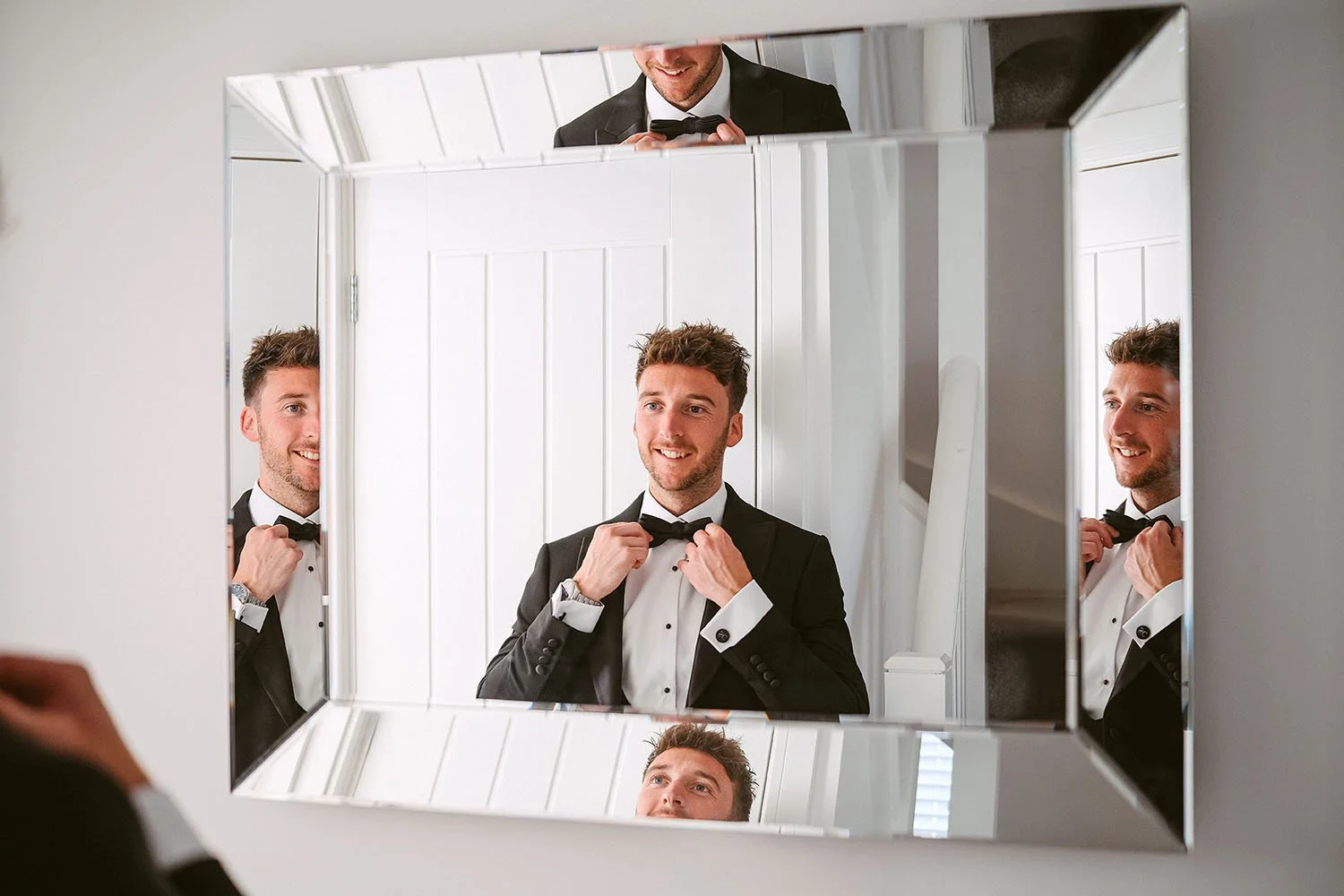 Groom adjusting his bow tie in a mirrored bathroom before his wedding