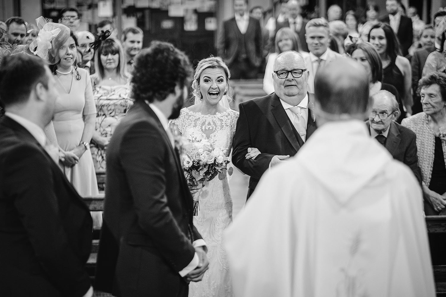 South Causey Inn wedding: bride laughing as she walks down the aisle on her father's arm while the groom waits, black and white