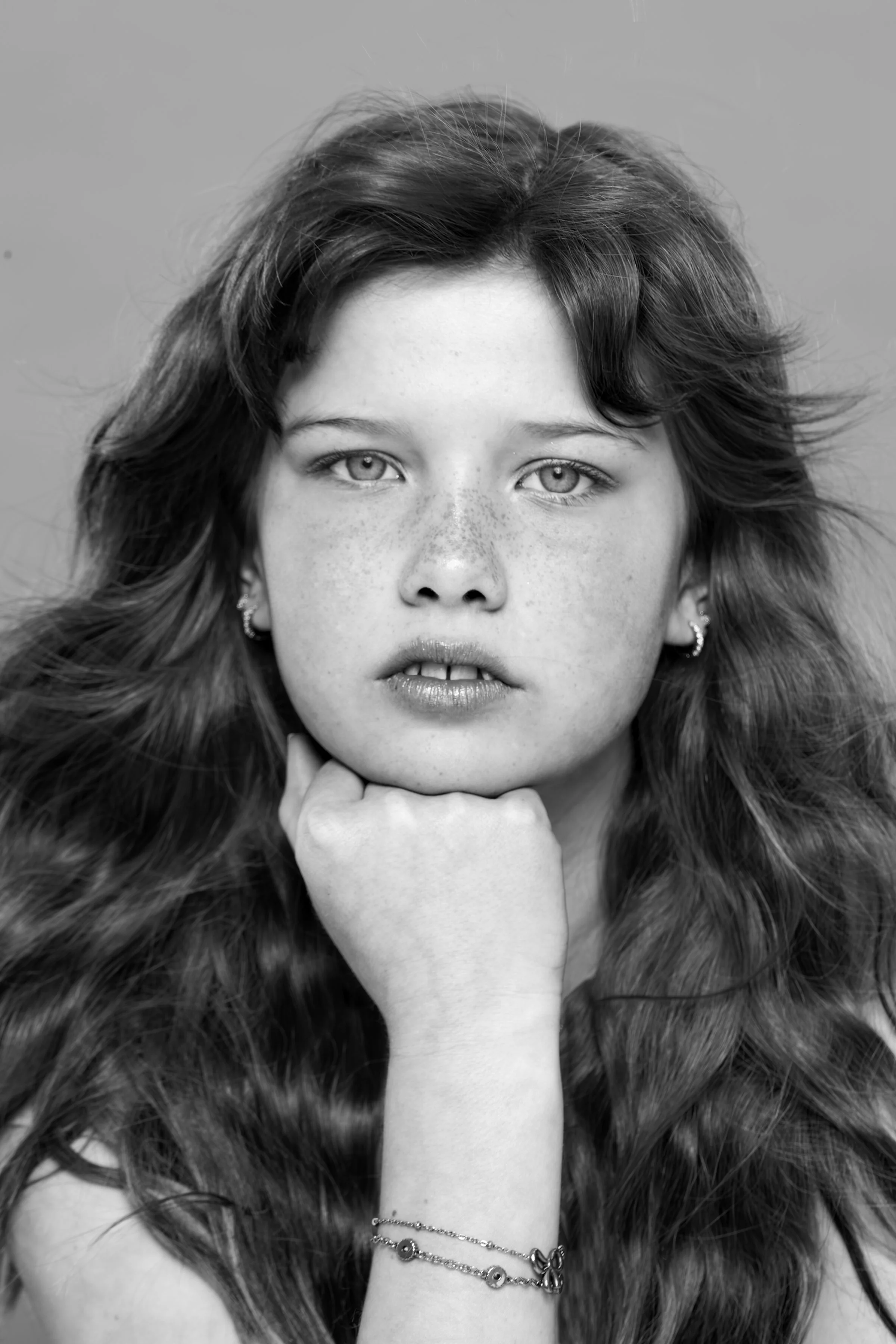 Black and white portrait of a young woman with long, wavy hair, resting her chin on her hand, looking directly at the camera.