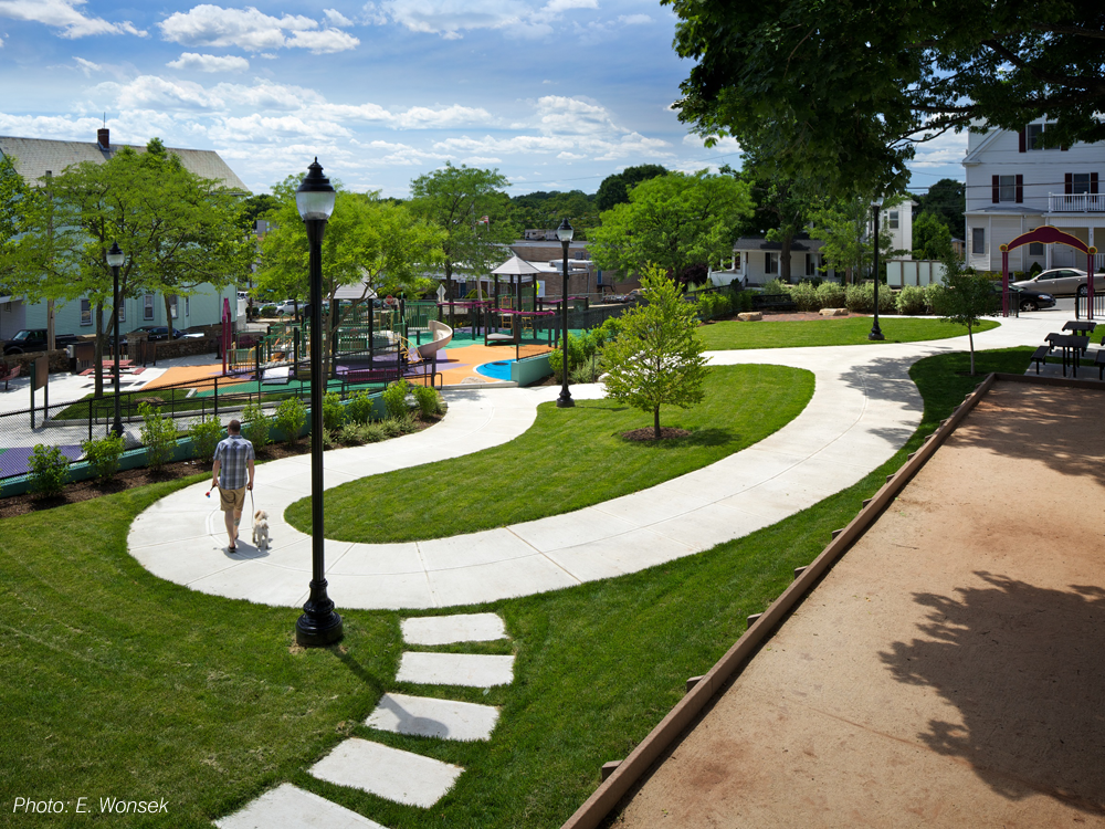 Formerly separated onto two levels, this park has been re-connected through our plan. An accessible route now links the refurbished play area and seating on the lower half, with a revitalized upper level that replaced an unusable basket-ball court with open lawn, a bocce court, picnic tables, and a winding pathway. Inspired by a recent mural on the uppermost wall, CBA's design uses the same vibrant colors, echoes similar shapes, and draws out details such as a blue bear's face to form the basis of the spray area.