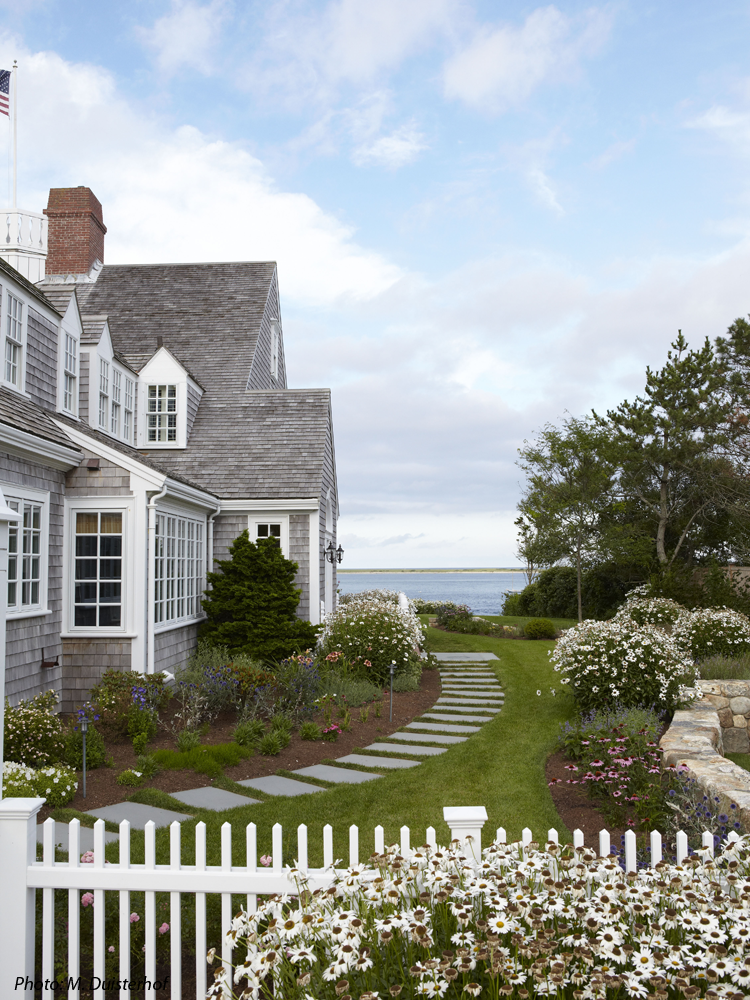 CBA created a beautiful landscape setting for this iconic home on Shore Road in Chatham which was featured in Country Living Magazine. The driveway was reconfigured to make a more inviting entrance that focuses on the house and the sea beyond. A field stone wall was designed to give the house and the immediate grounds a base on which to rest. A picket fence lined with roses defines the foreground of the house. Bluestone stepping stones welcome the guests through the arbor to the main door at the side of the house. Colorful, easy care perennials surround the house and an elevated patio at the rear of the house offers spectacular views. 